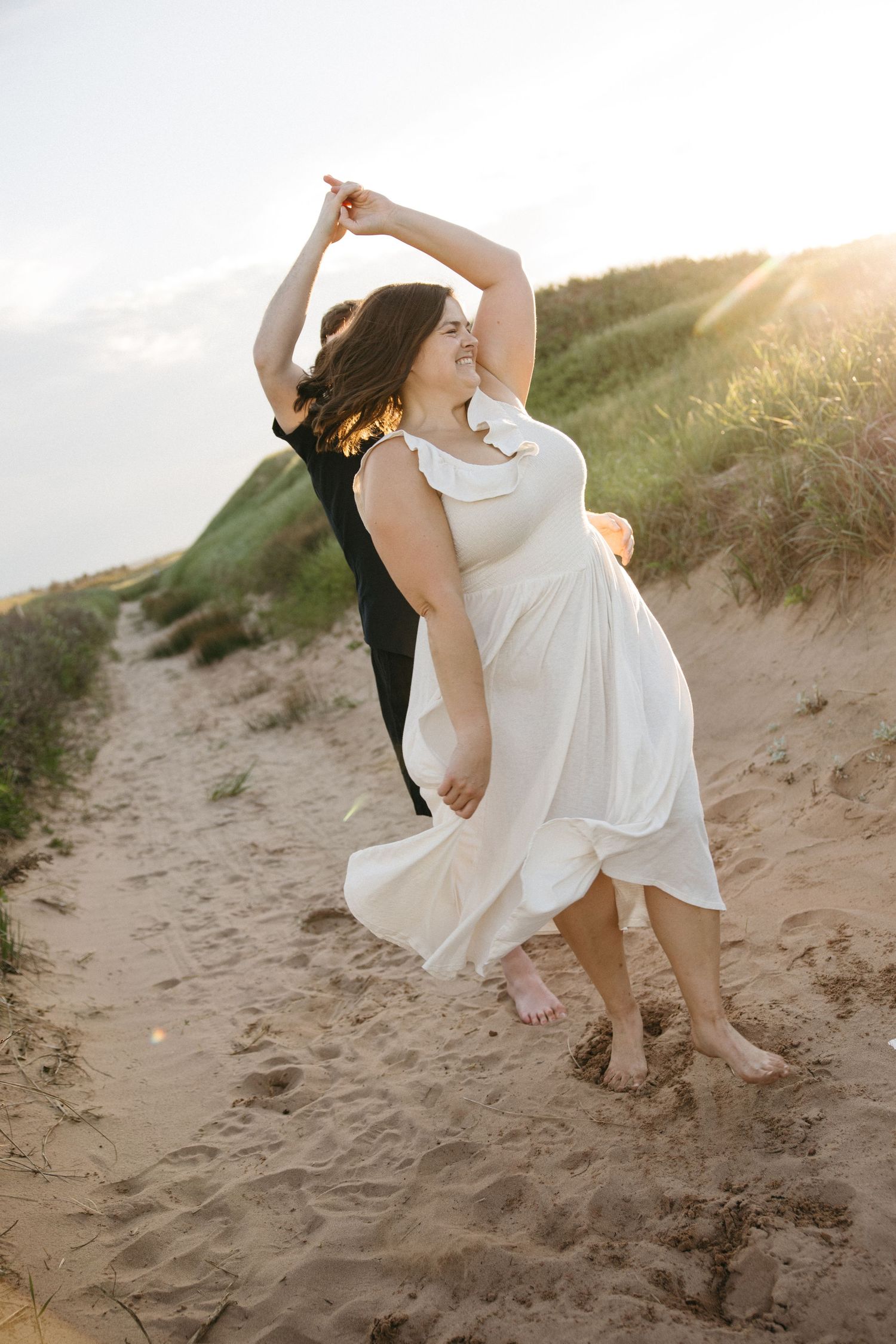 Couple dancing joyfully on sandy beach dunes at golden sunset.