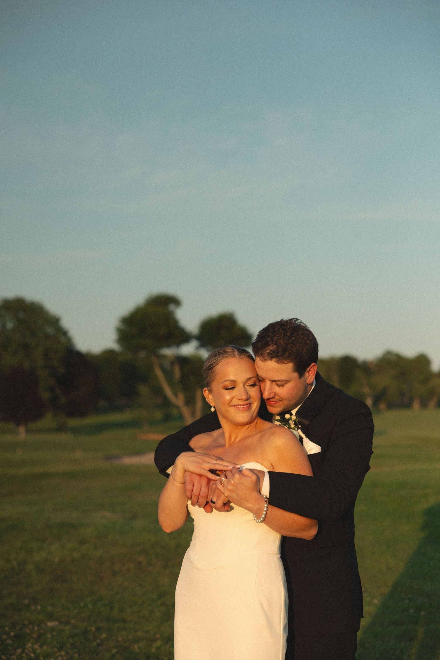 Couple embraces in warm evening light on a golf course.