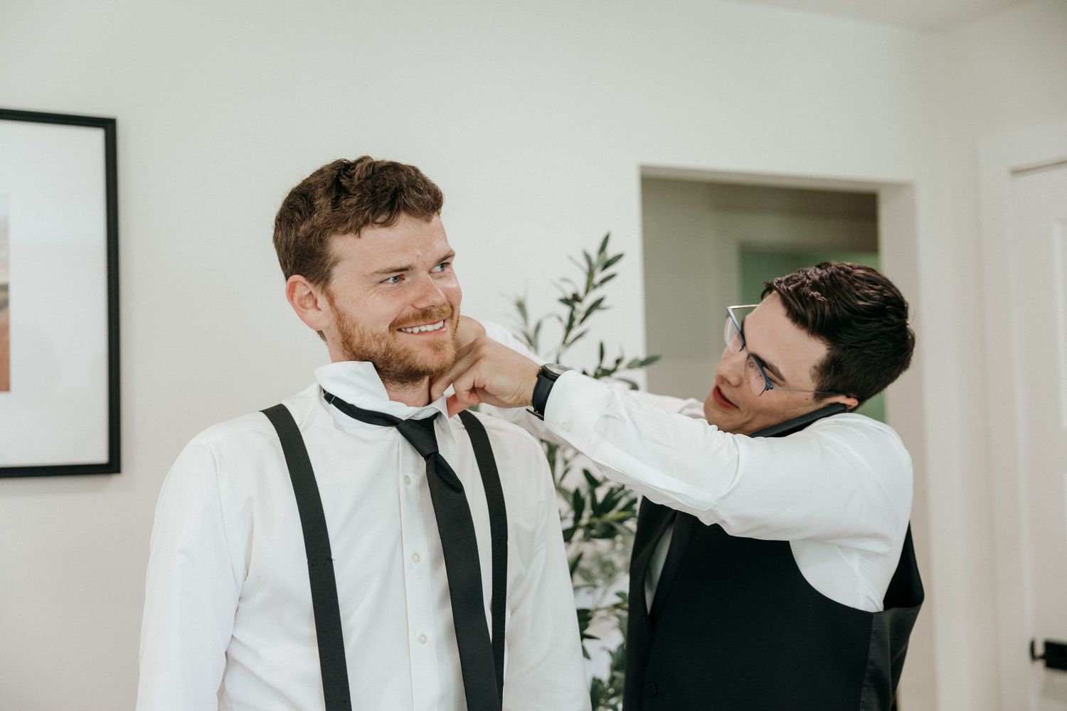 Wedding party members in formal attire prepare together in a bright white room.