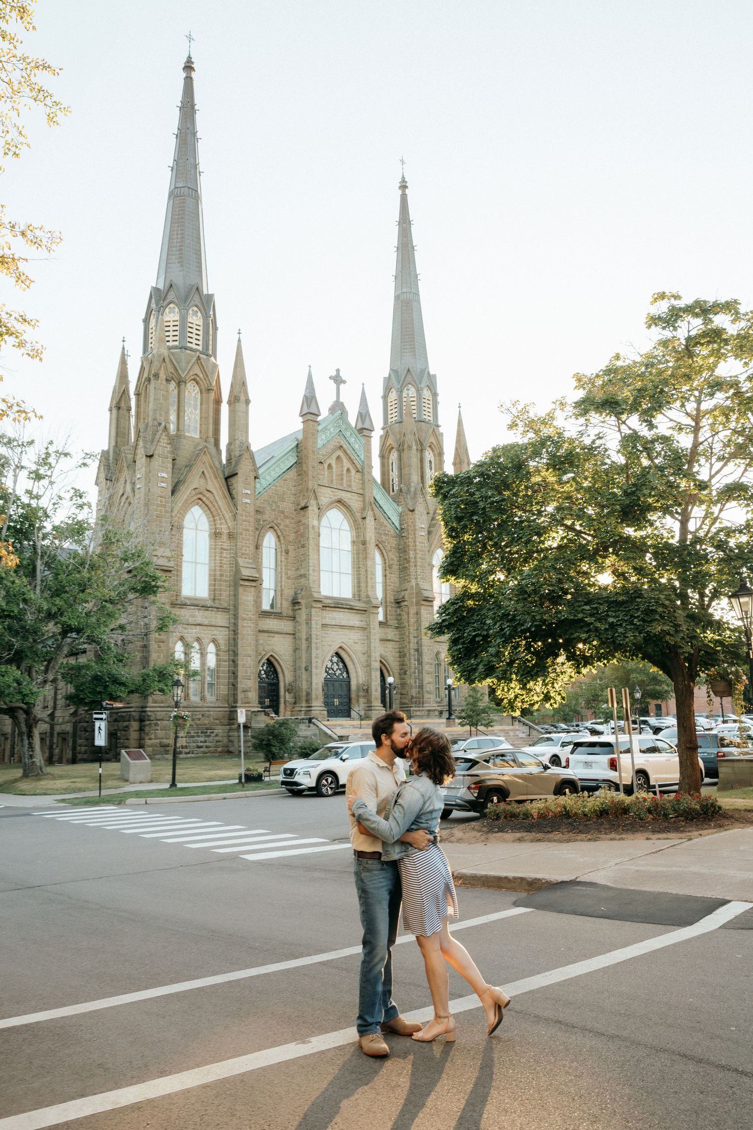 A couple shares a romantic moment in front of a gothic cathedral with tall spires at sunset.