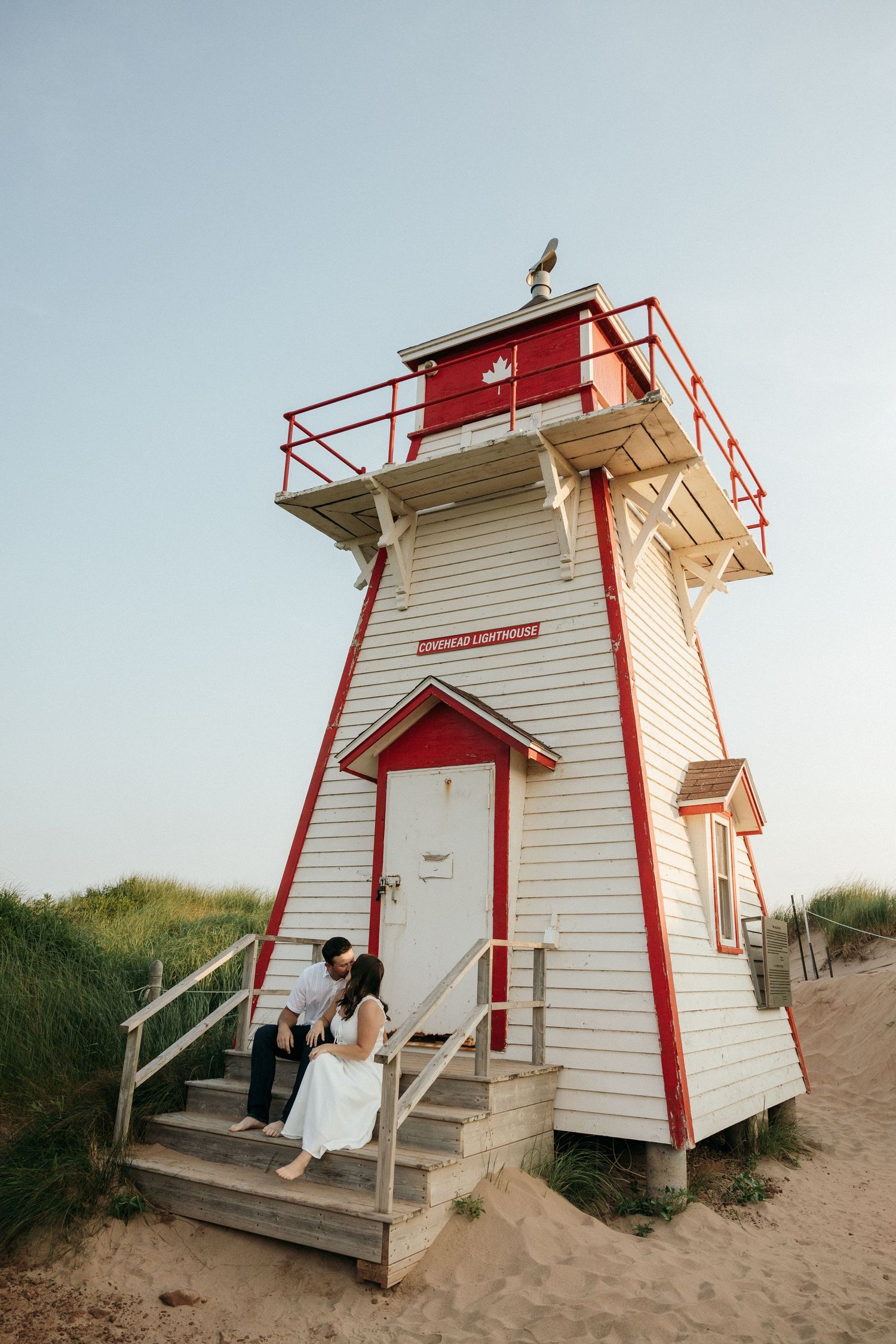 A scenic view of a couple sitting on the steps of a red and white lighthouse.