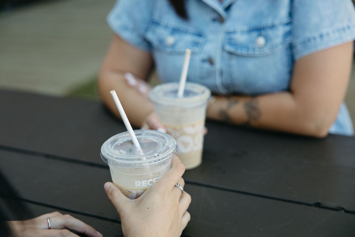 Close-up of iced drinks with straws on a dark wooden table surface.