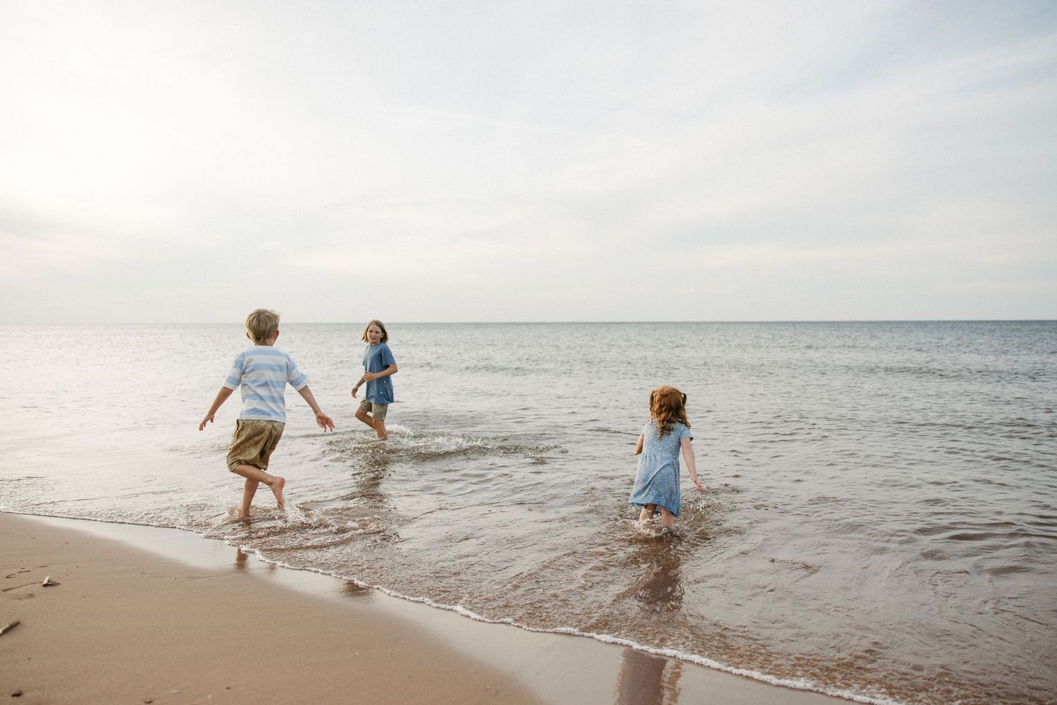 Three children playing in ocean waves on a sandy beach during a family vacation.