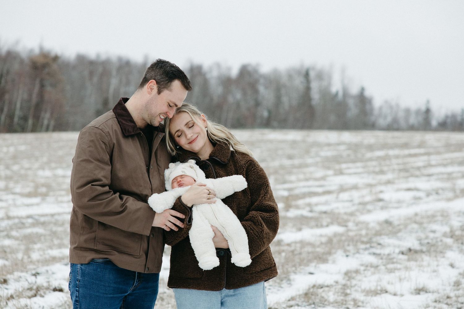 A family of three shares an intimate moment in a snowy winter field.