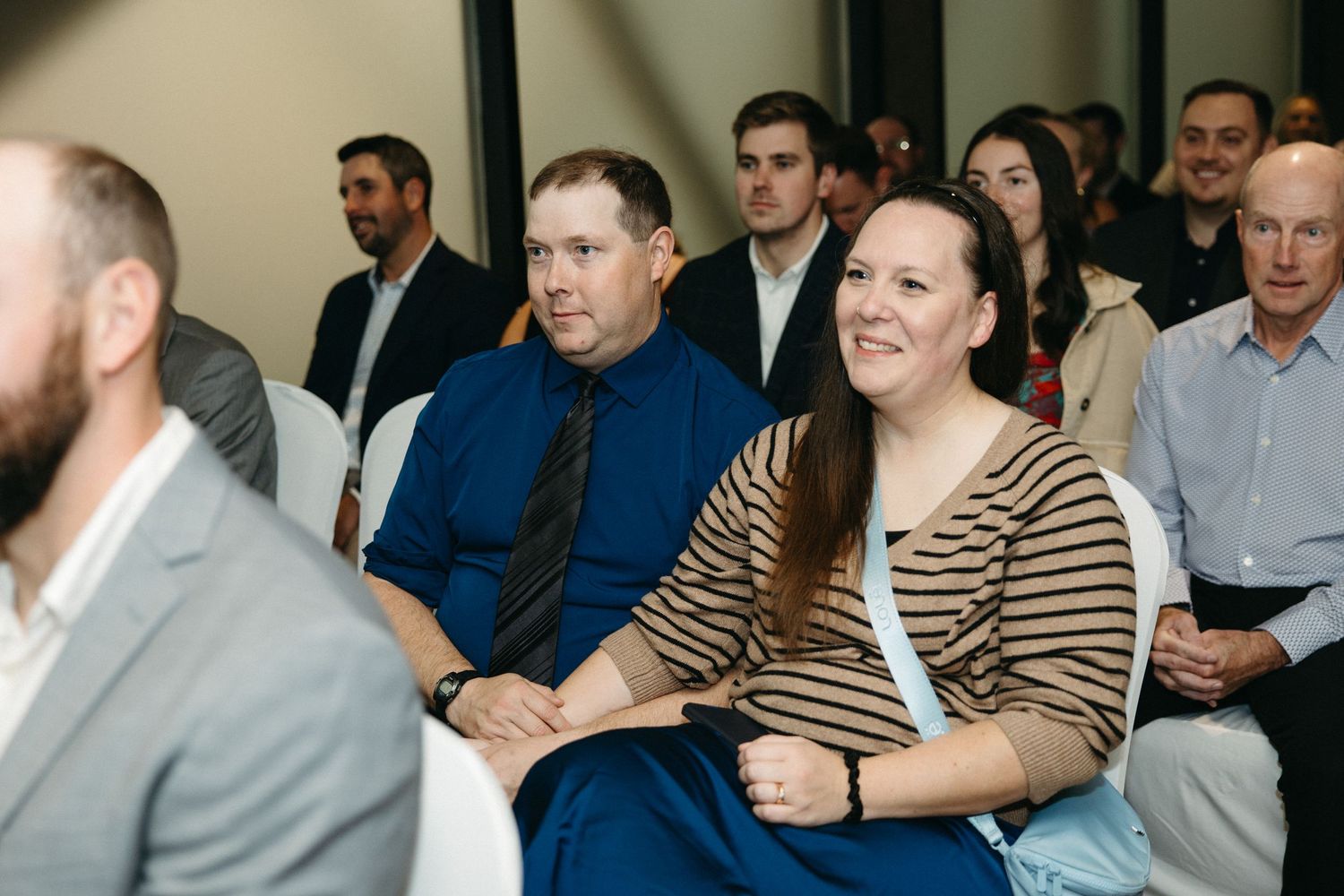 Audience members smile while seated in rows during an indoor event.