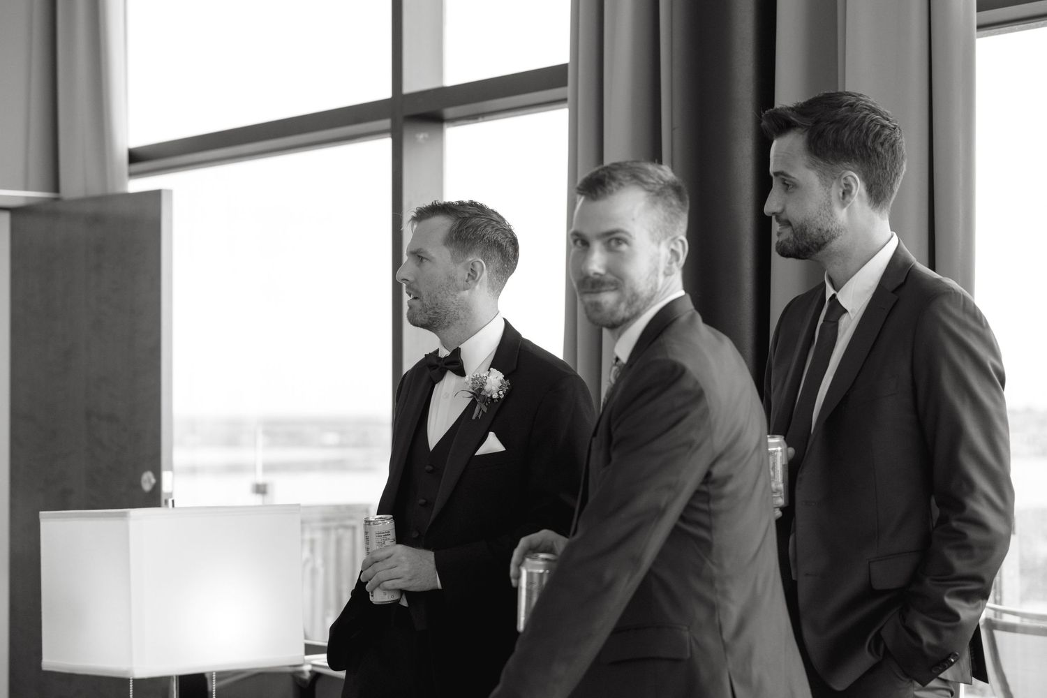 Silhouettes of formally dressed guests gathered by large windows at an event.