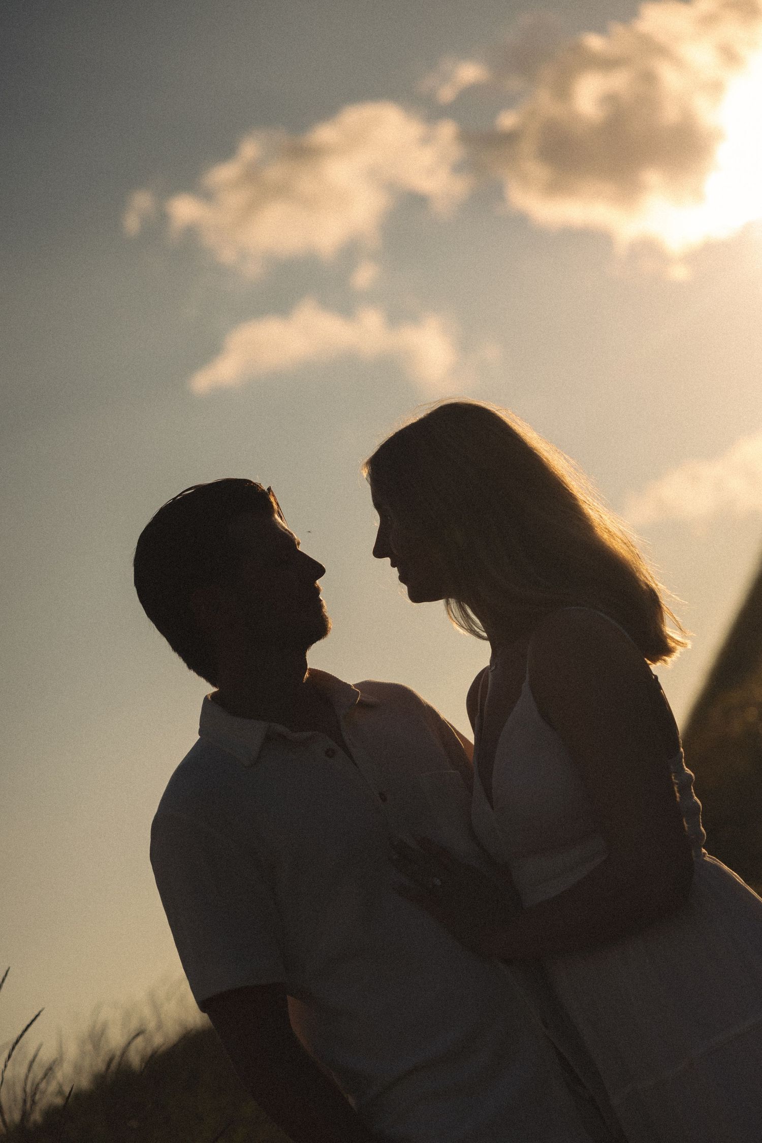 Romantic couple silhouette embracing at sunset with golden sky and clouds in background.