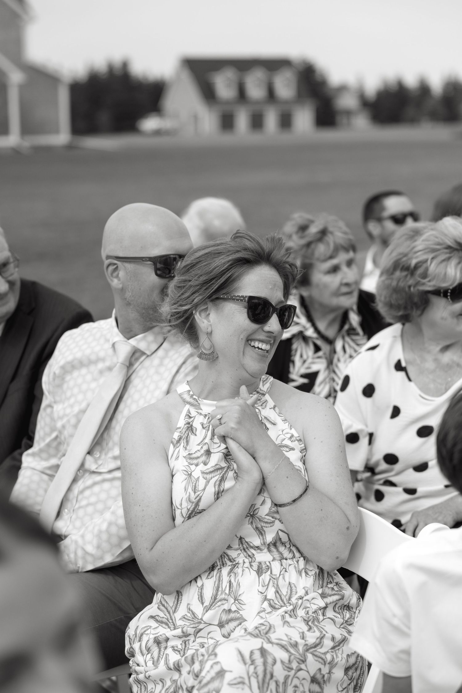 Black and white photo of wedding guests laughing and smiling during an outdoor ceremony.