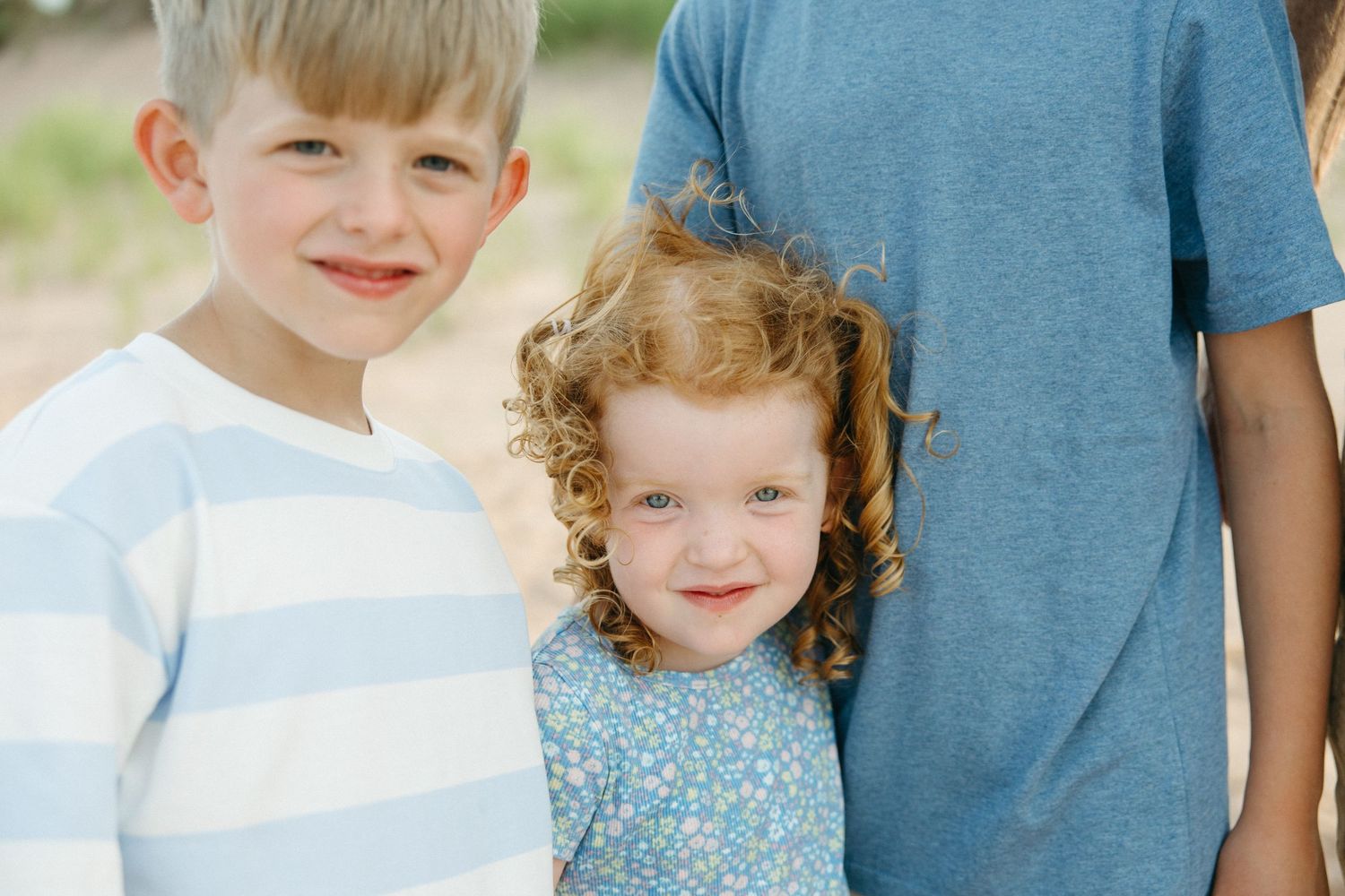 Two young children, a blonde boy and curly red-haired girl, posing at beach.