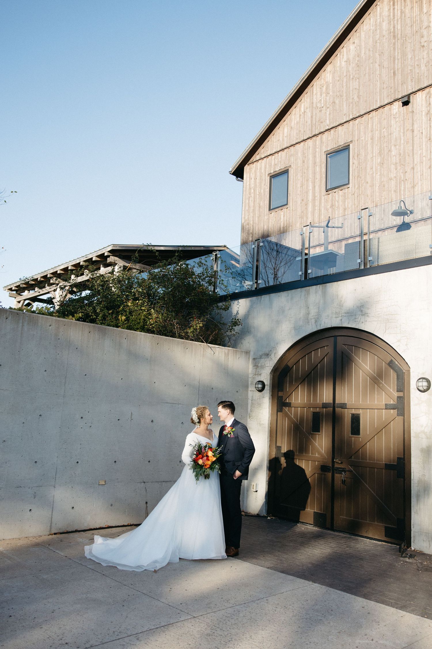 Wedding couple poses against modern concrete architecture and wooden barn doors.