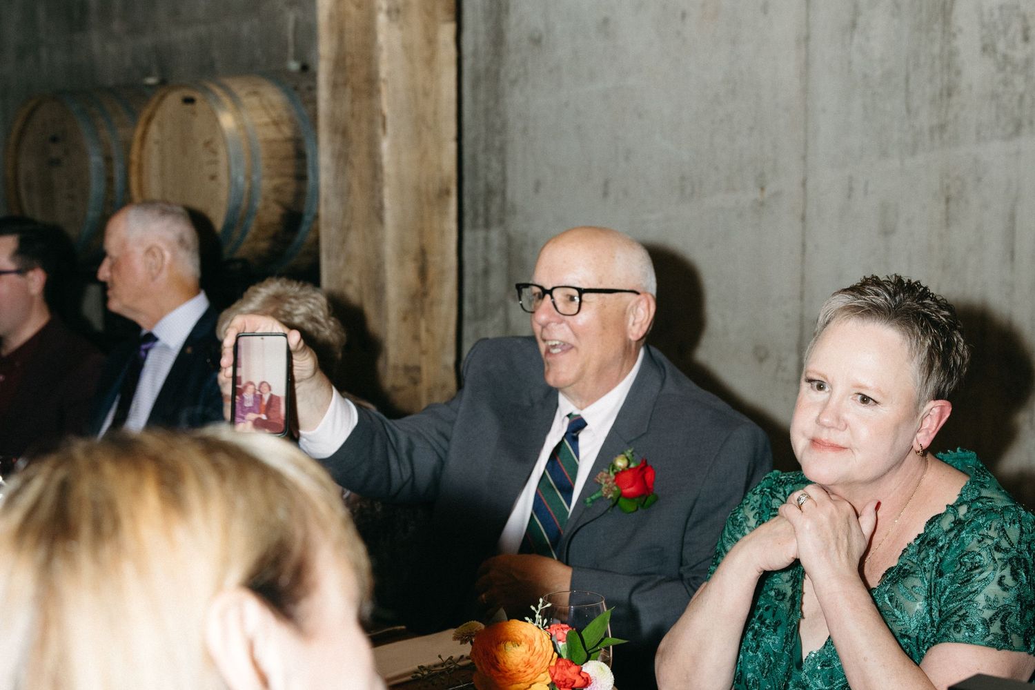 Guests seated at tables in a rustic venue with wine barrels visible in background.
