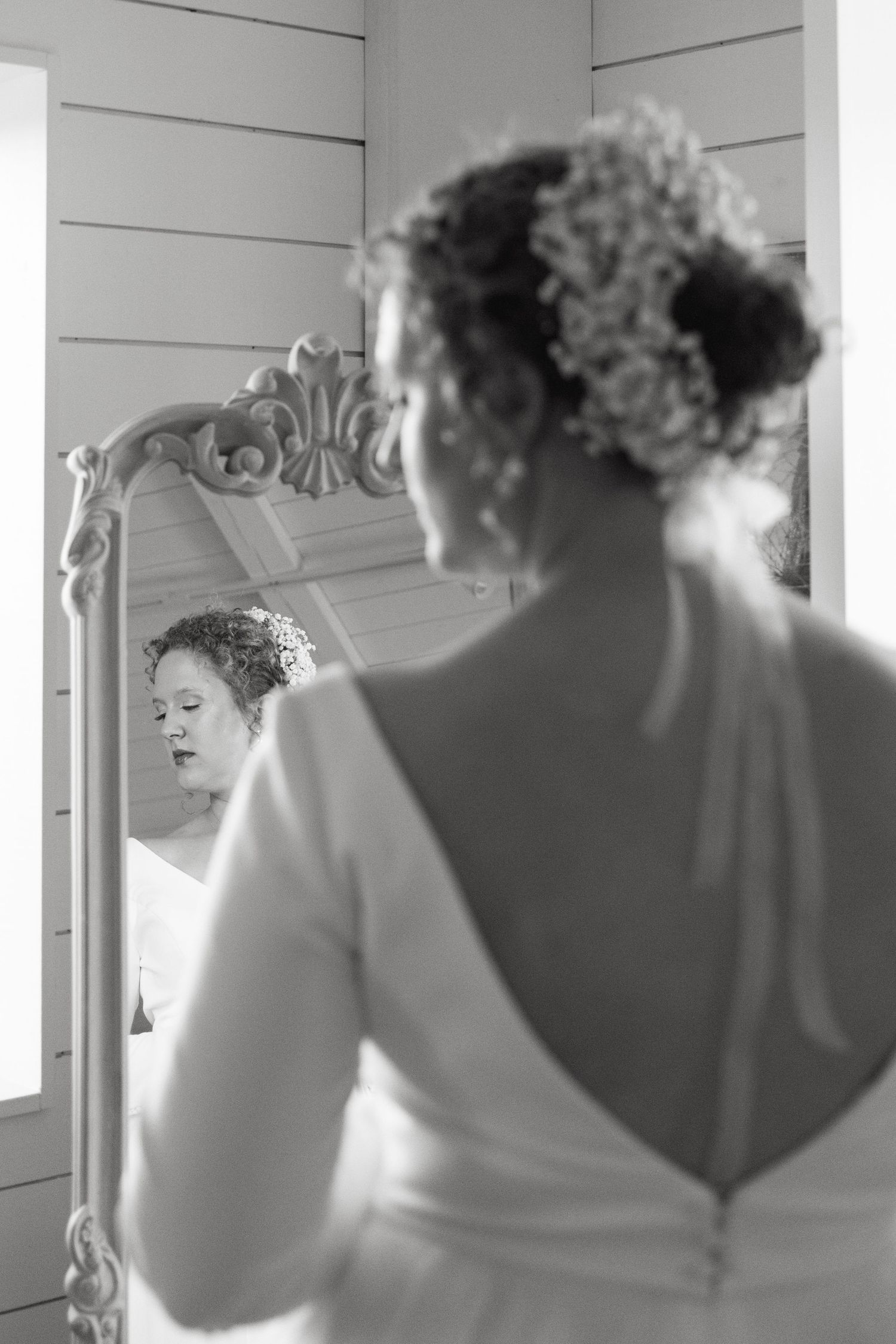 A reflection in an ornate white mirror shows a bride getting ready for her wedding day.