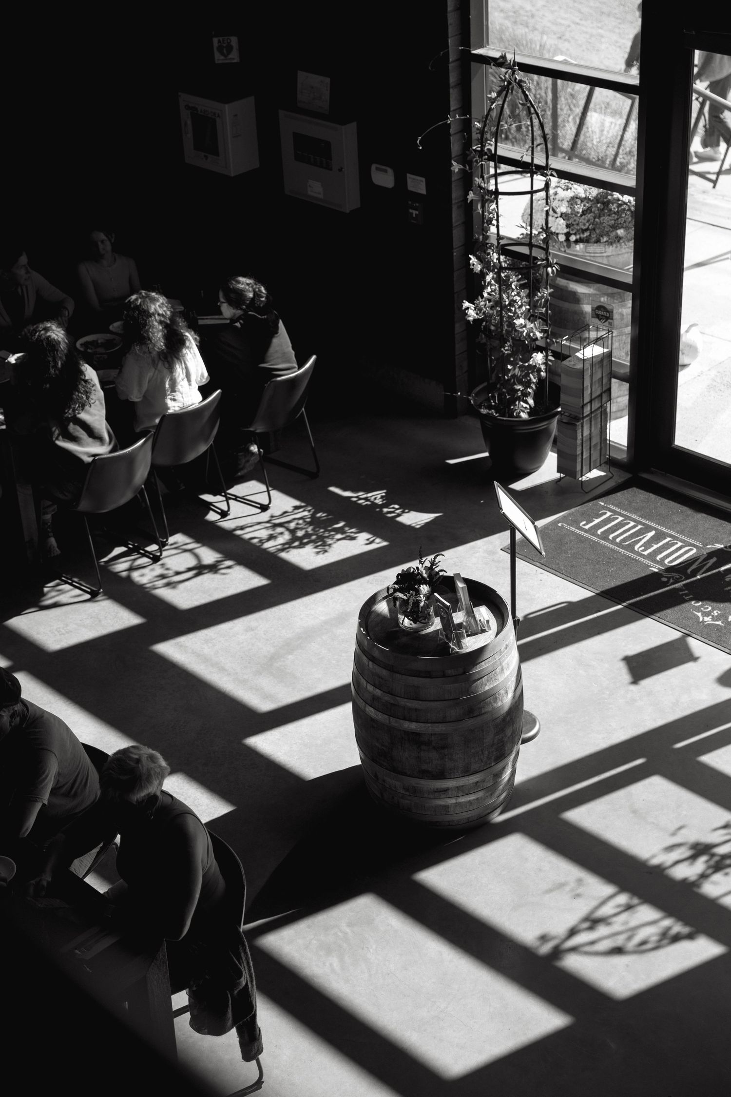 Dramatic black and white photo of sunlight casting window shadows across a room with people sitting.