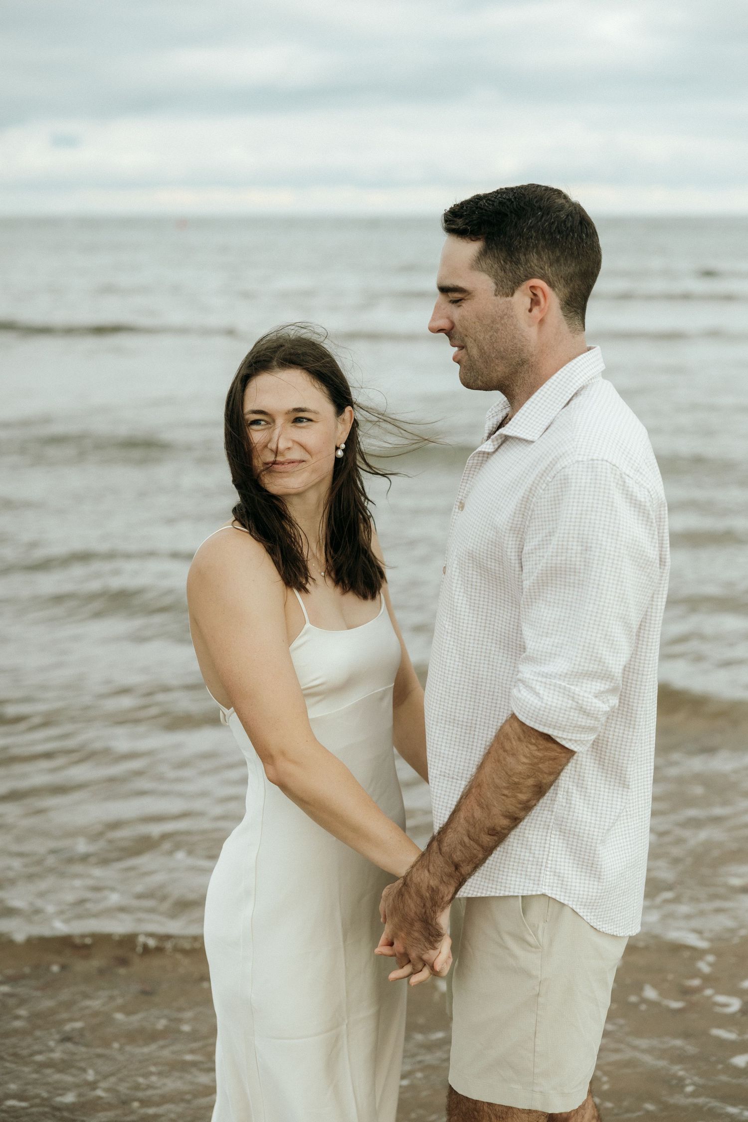 A romantic beach photoshoot featuring a couple in white attire against the ocean backdrop.