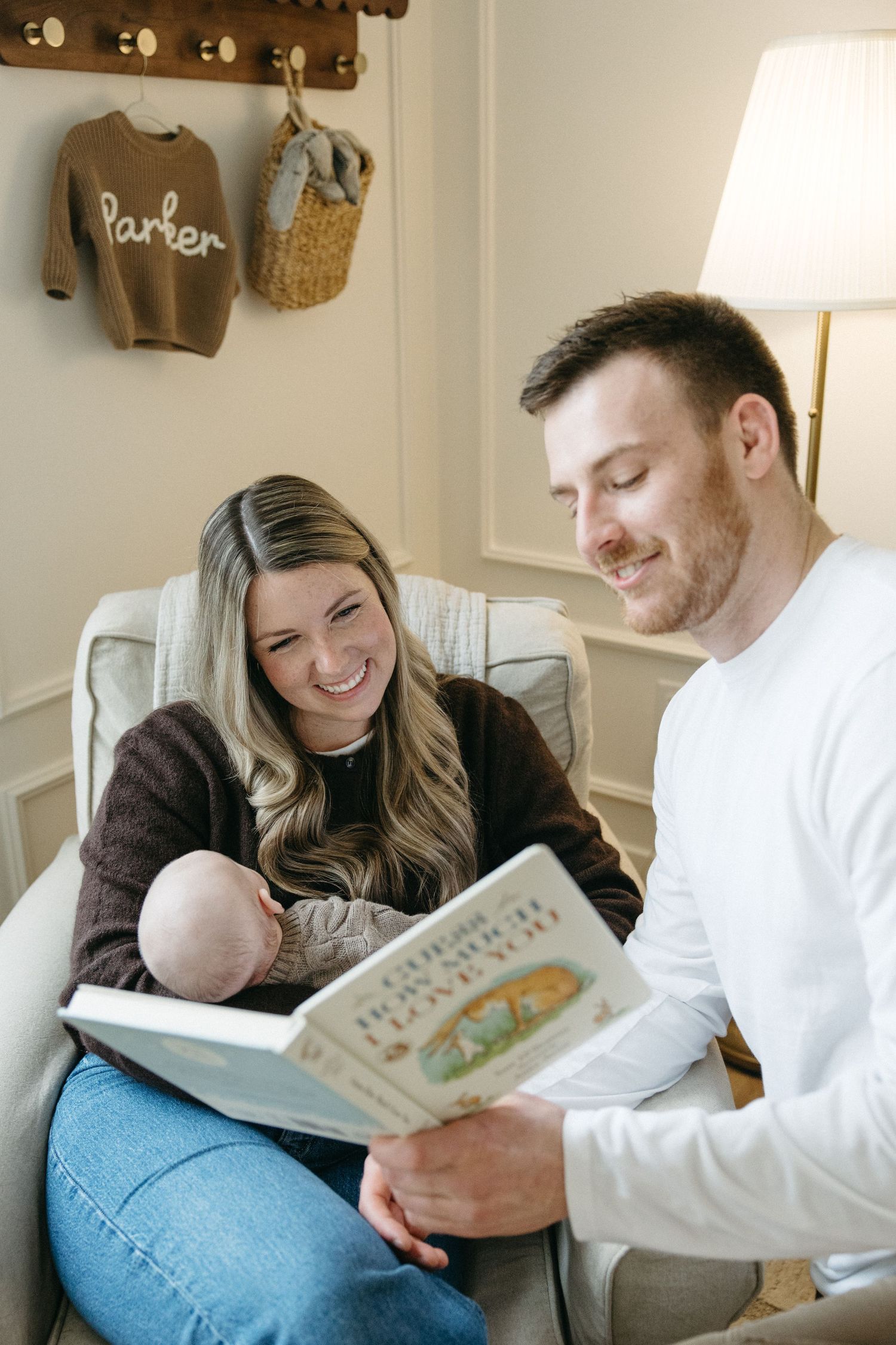 A cheerful reading session in a cozy nursery corner with wall-mounted baby clothes and decor.