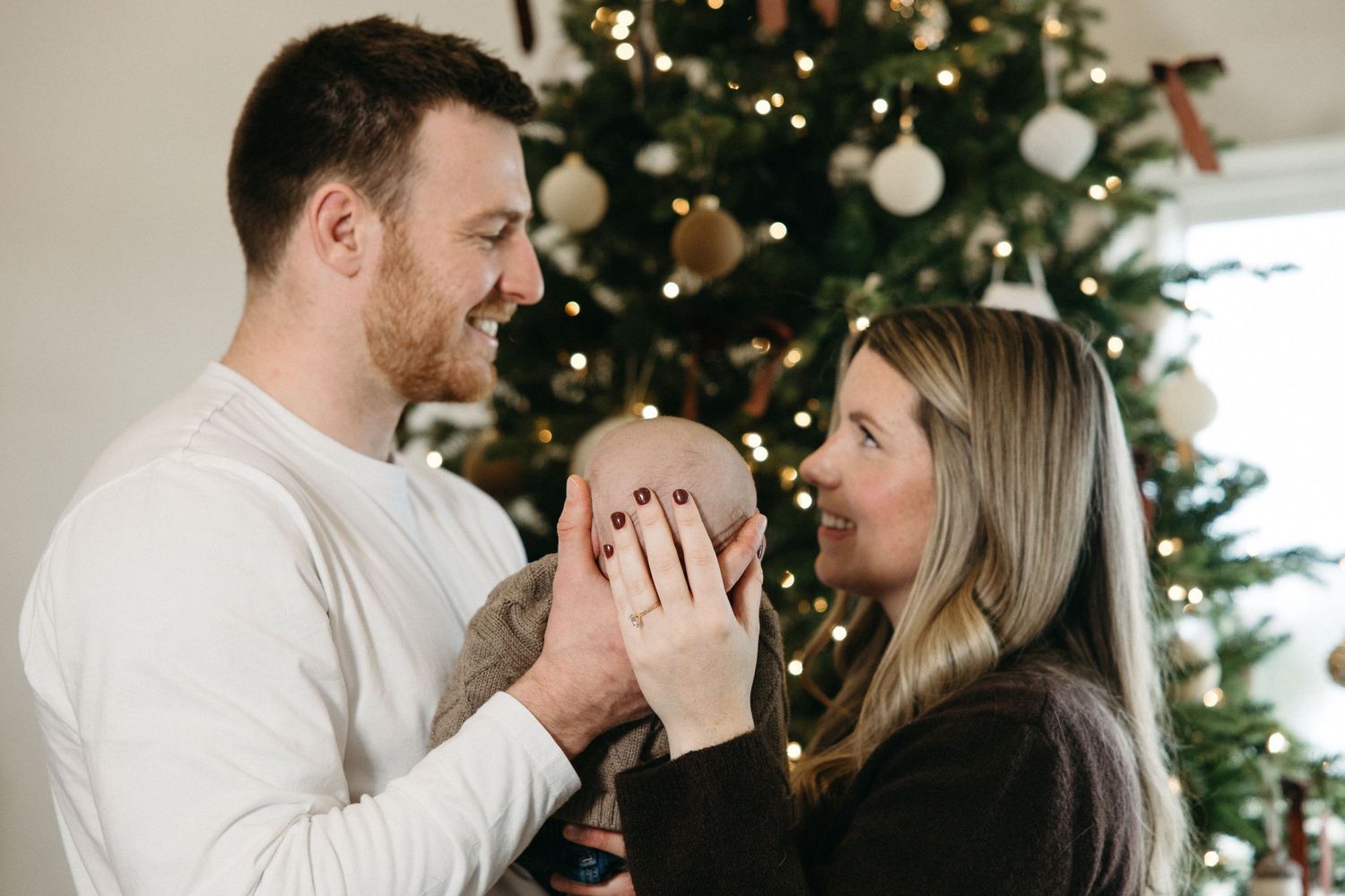 Family sharing loving moments together in front of decorated Christmas tree with white ornaments.