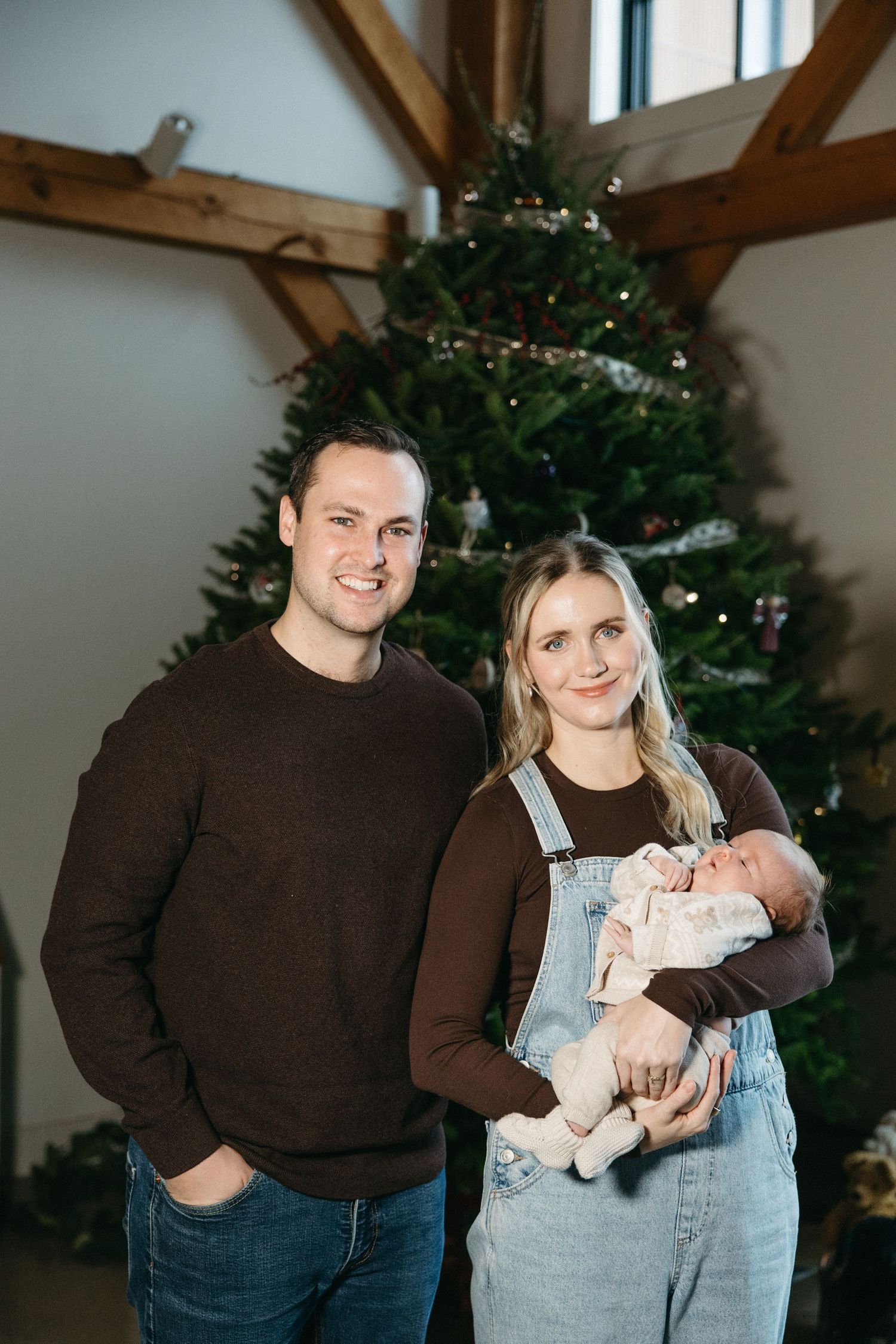 Family posing for holiday portraits in front of decorated Christmas tree in rustic room.