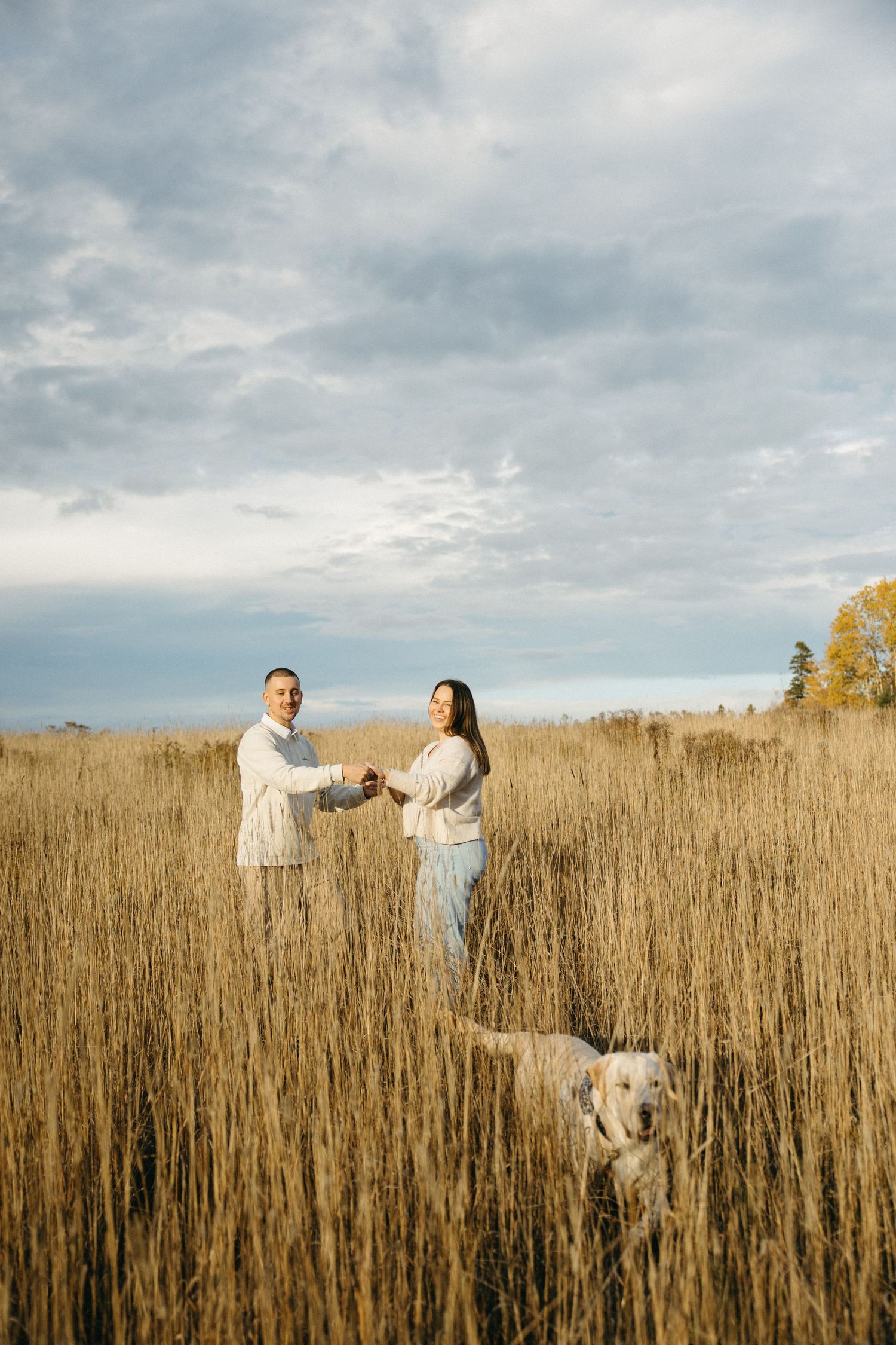 Couple enjoying a playful moment in a tall grass field during golden hour.