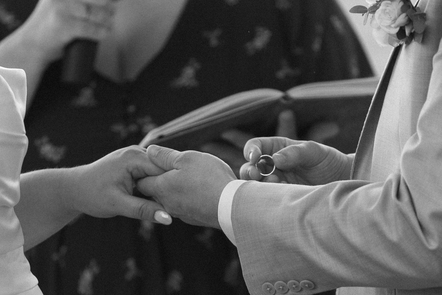 A black and white close-up of hands exchanging wedding rings during a ceremony.