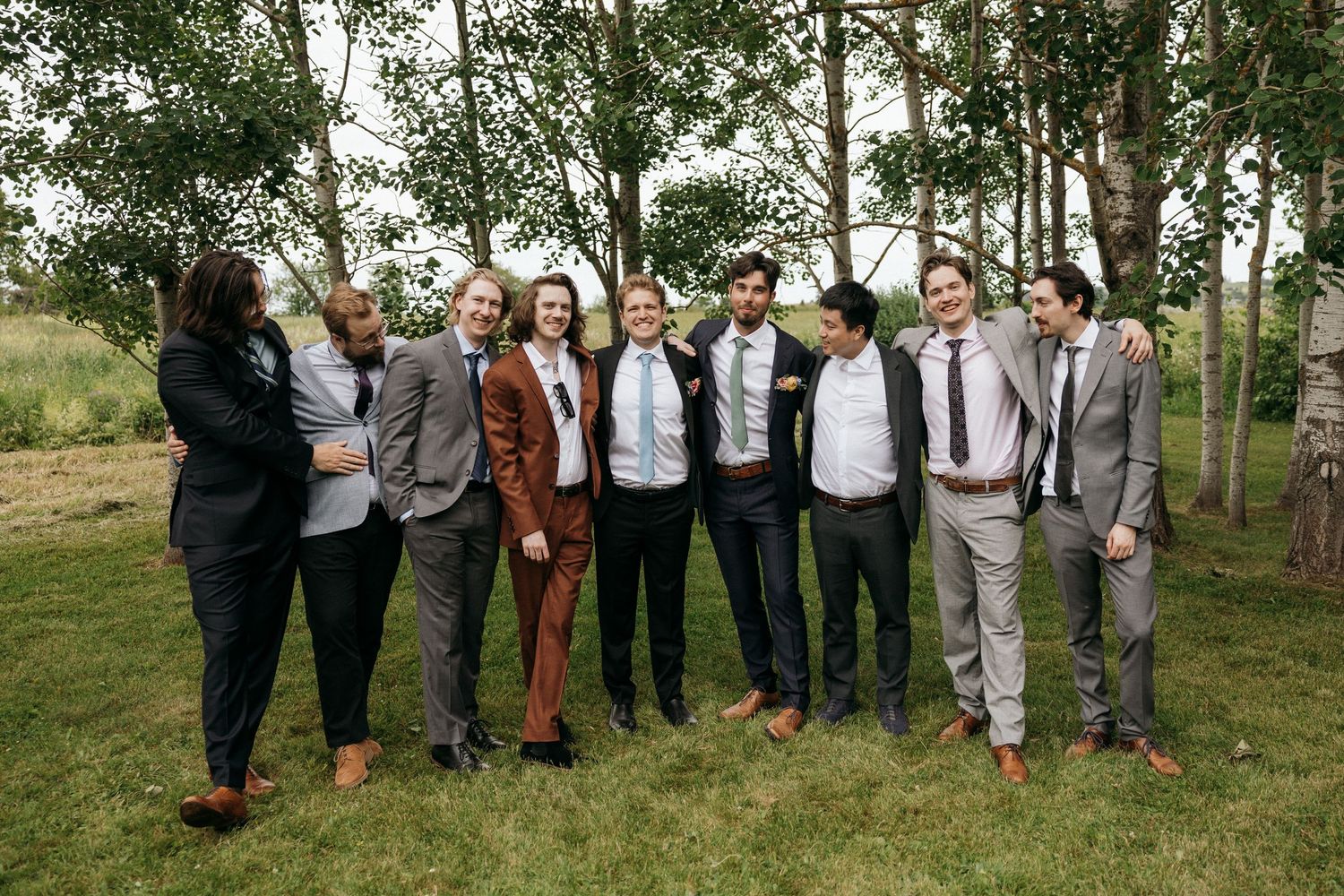Large wedding party group portrait taken outdoors with trees in background.
