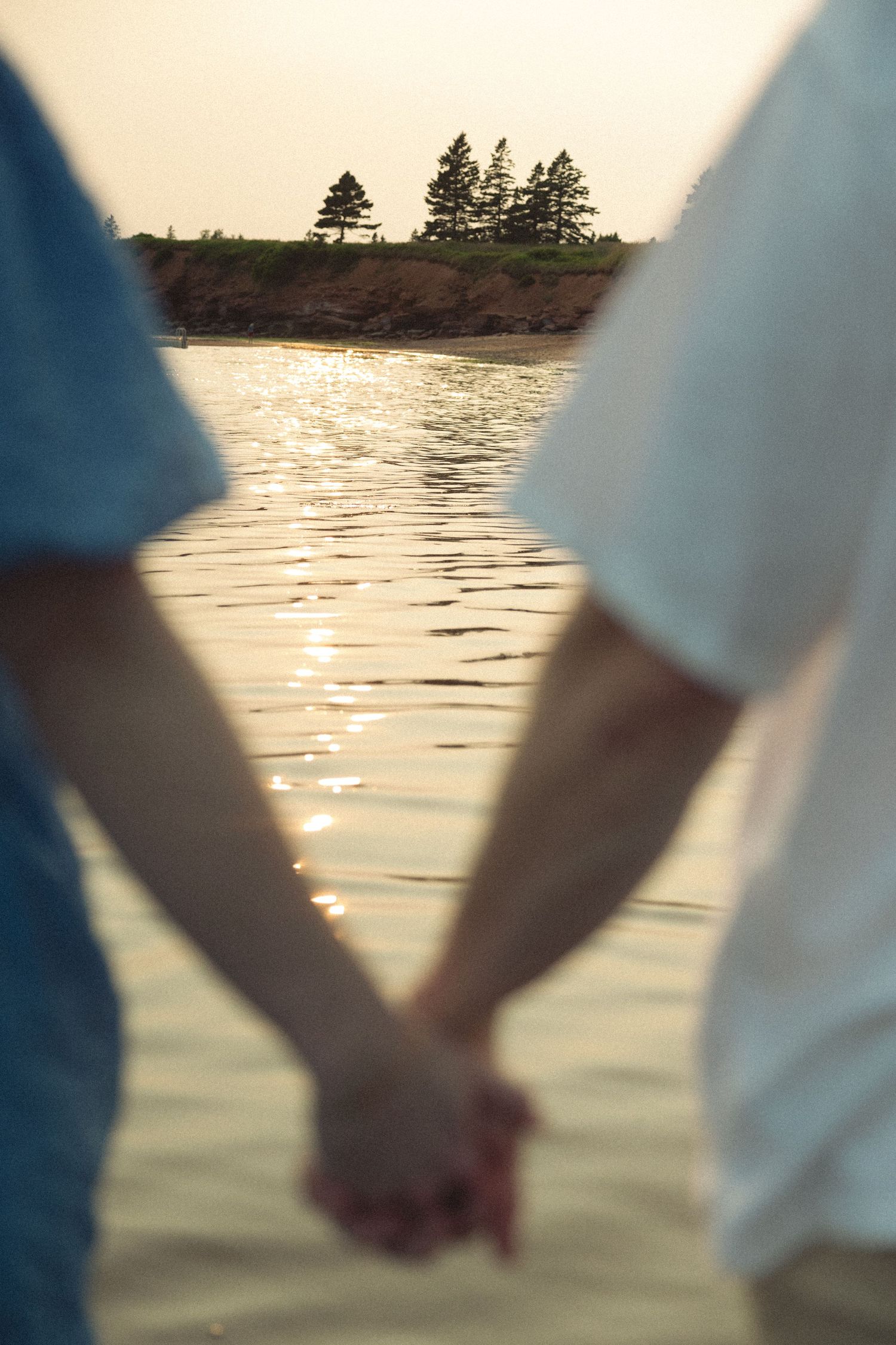 Silhouetted hands hold together against a golden sunset over the water.