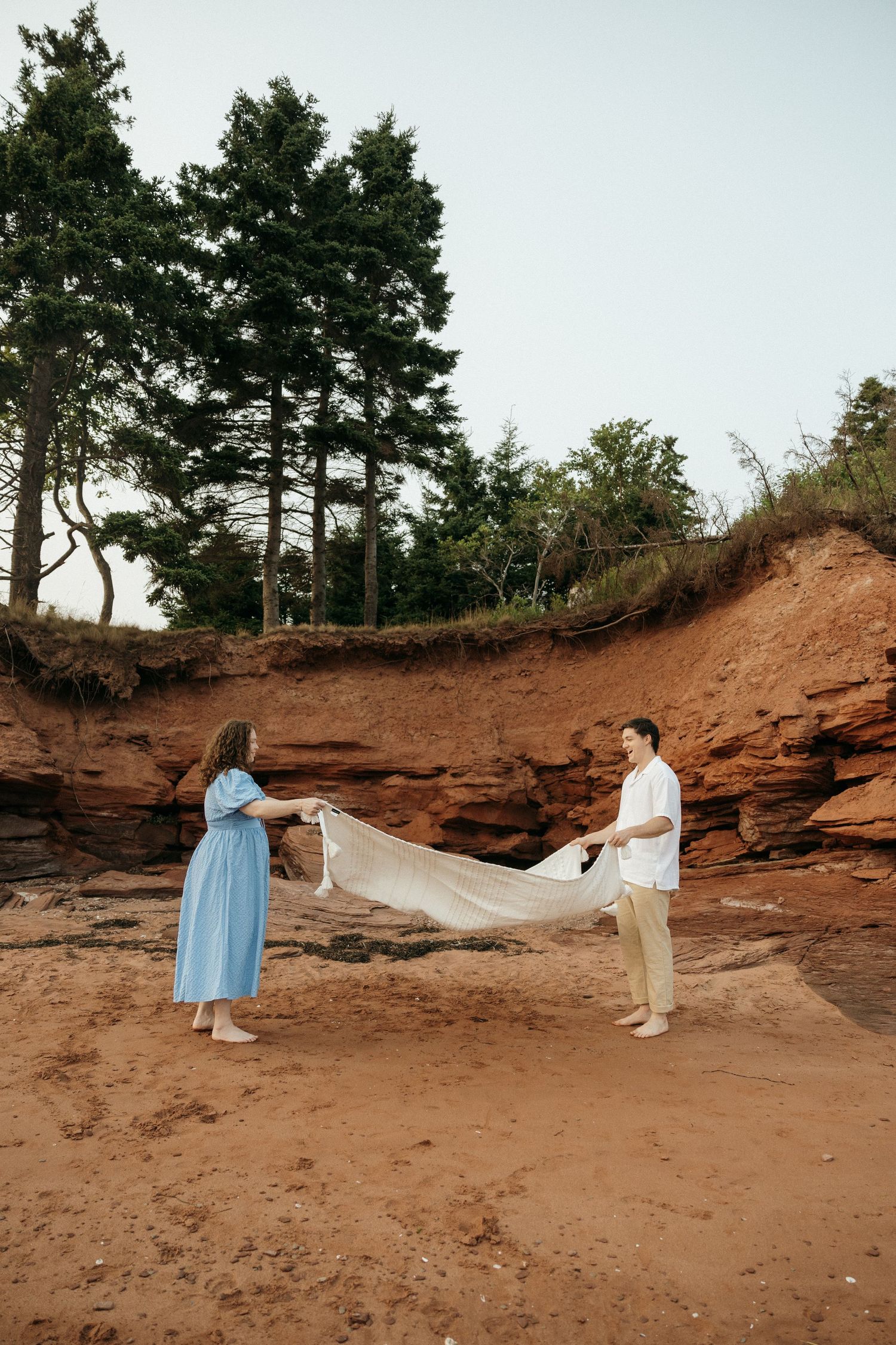 Couple having their photos taken on sandy terrain with red rock formations and trees above.