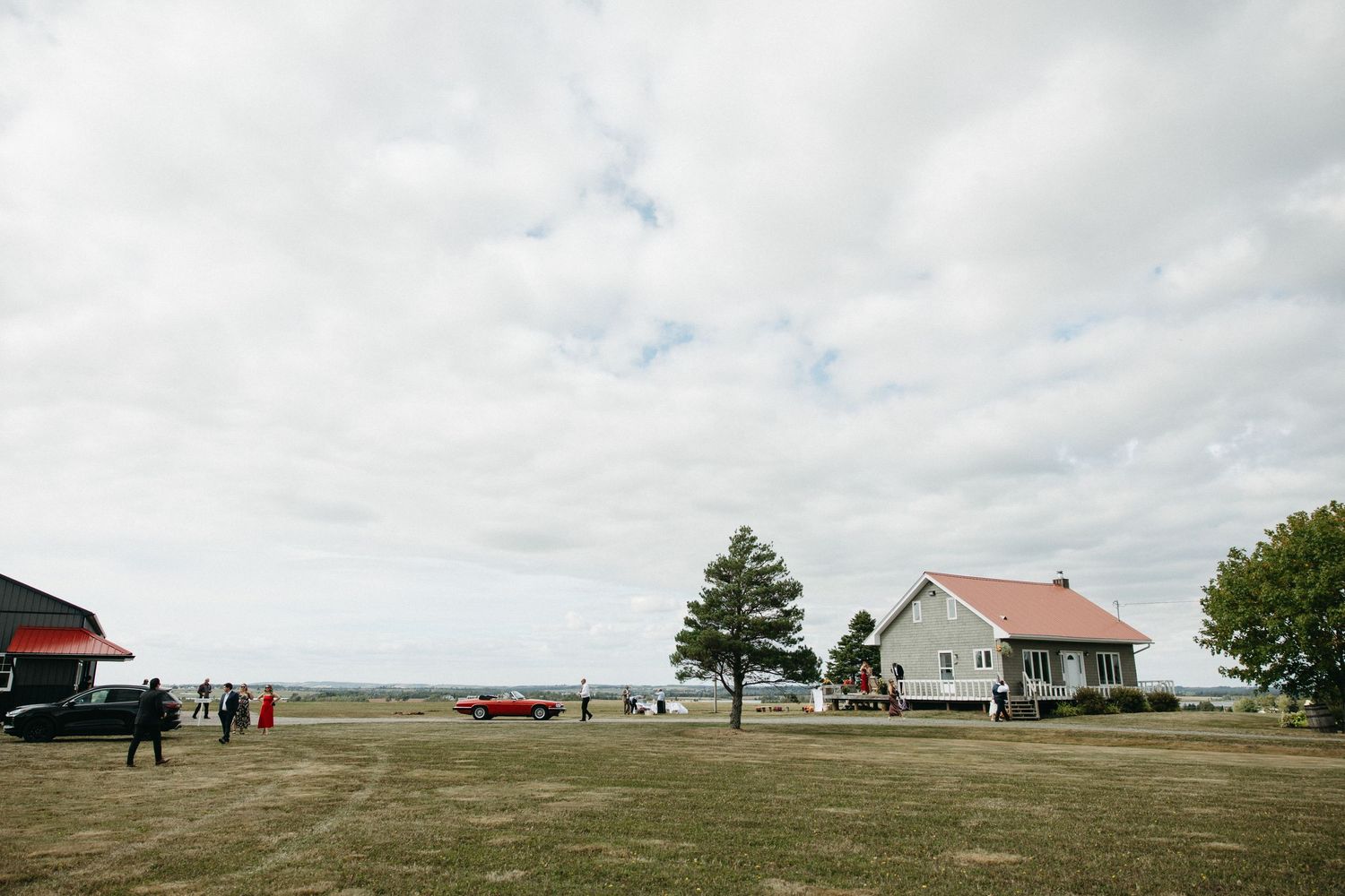Panoramic view of a rural landscape with buildings and vehicles under cloudy skies.