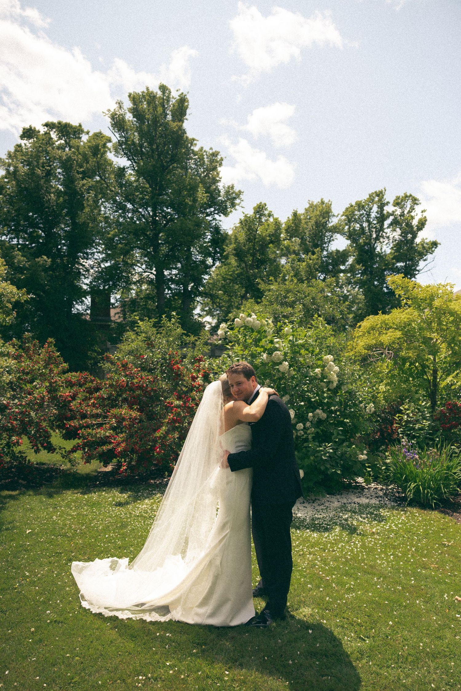Wedding couple dancing in a sunny garden surrounded by trees and wildflowers.