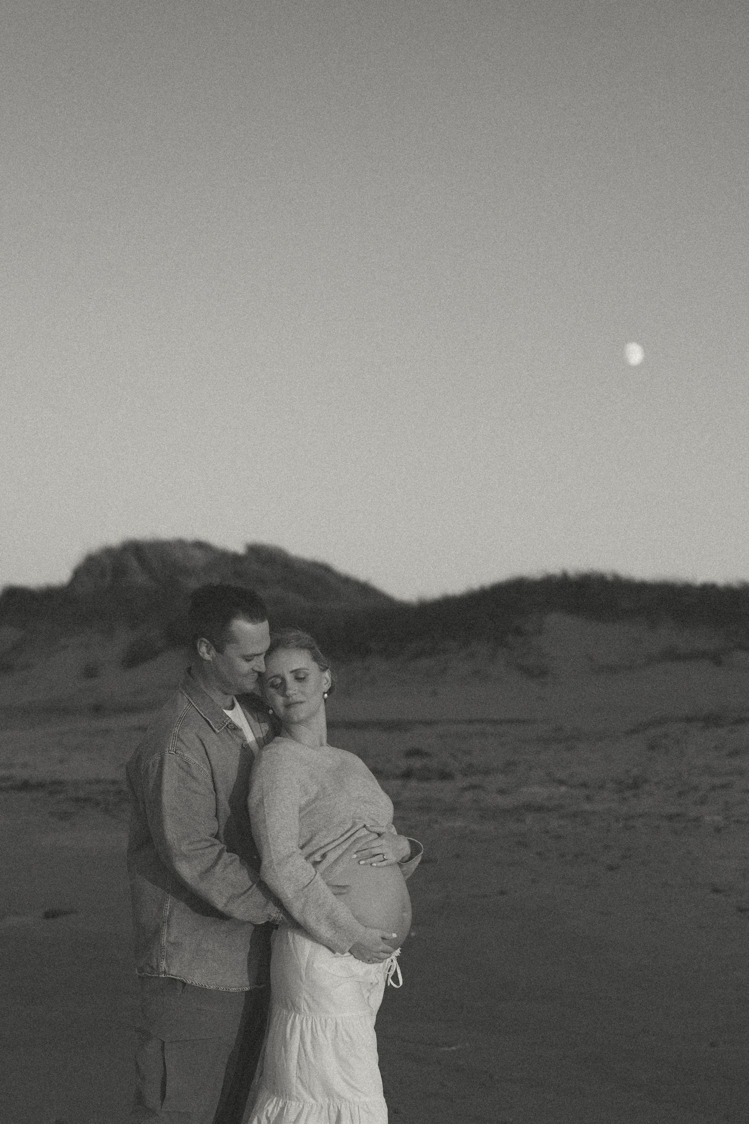 A monochrome maternity photo with mountains and moon in the background.