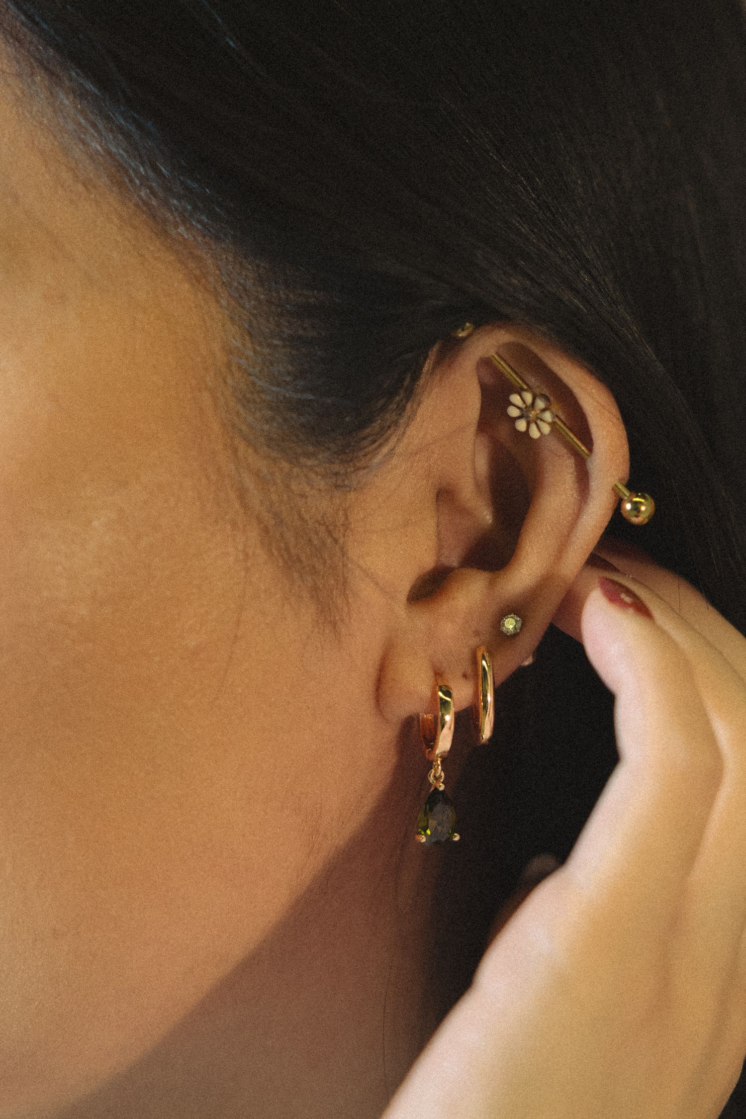 Close-up series of gold ear piercings and jewelry against a dark background.