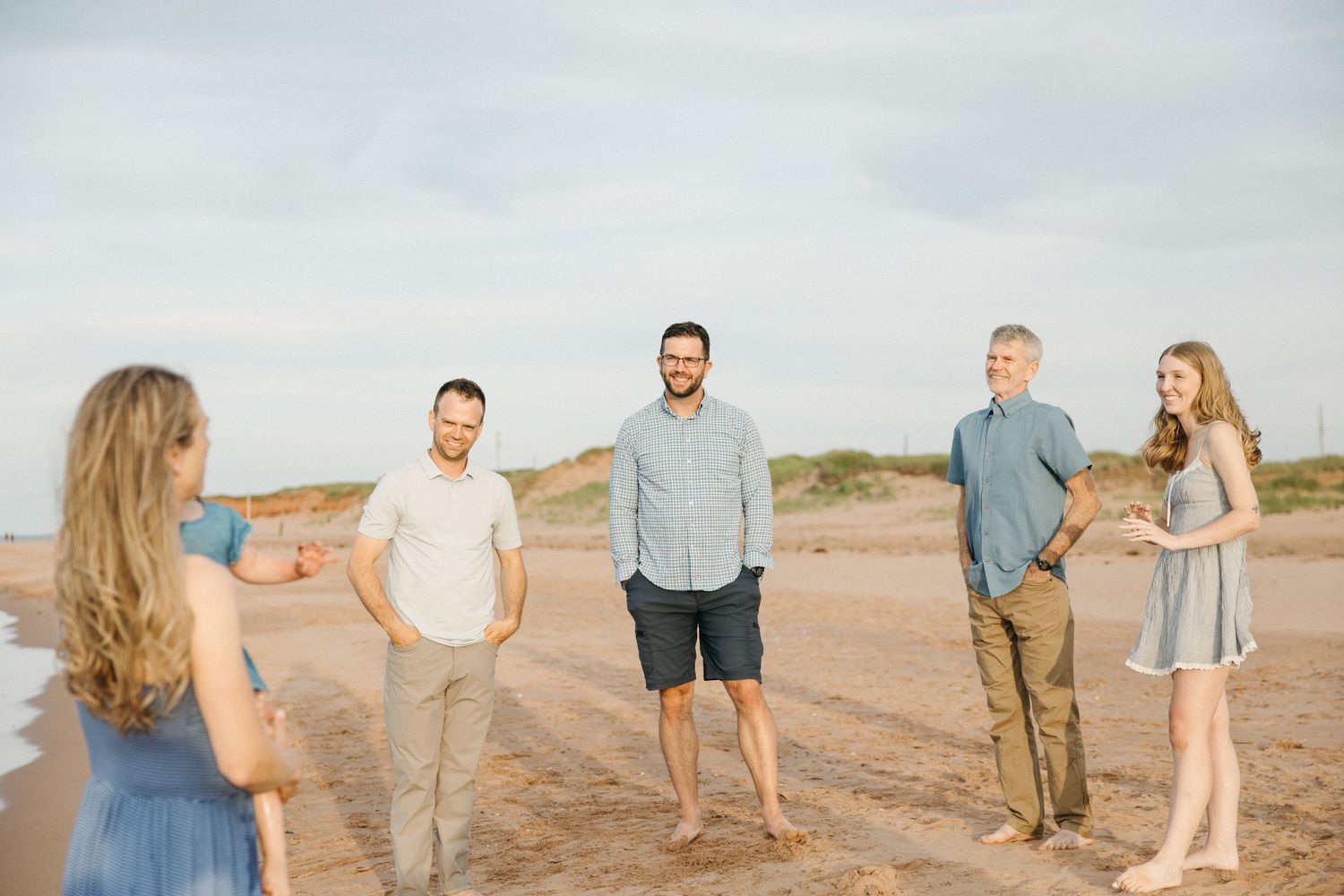 Five people enjoying a casual beach gathering on sandy shores with dunes in the background on a sunny day.
