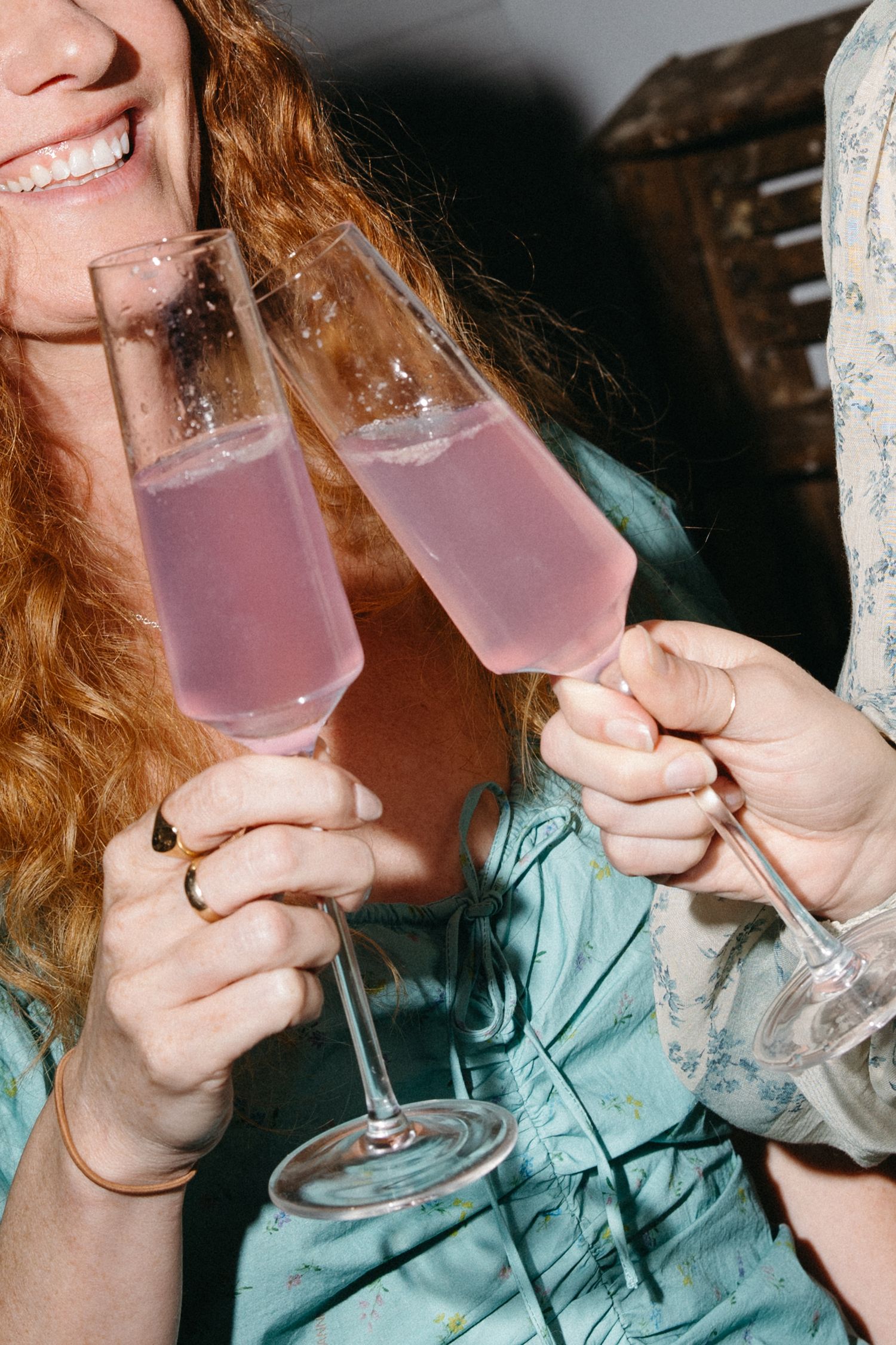 Two women clinking pink champagne flutes together in a celebratory toast at a party.