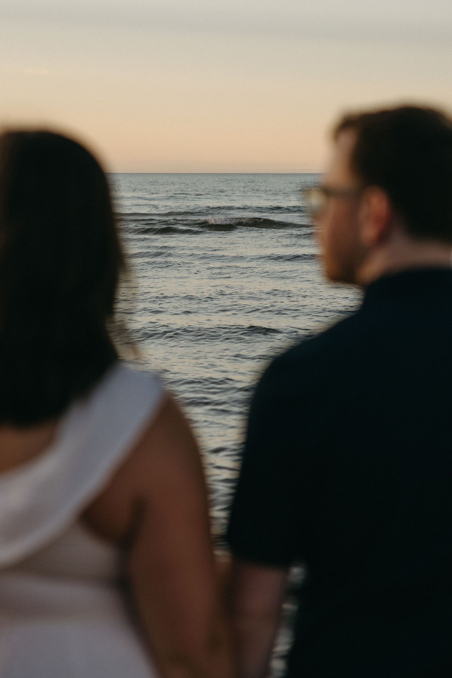 Couple standing together gazing at calm ocean waves during a serene sunset.