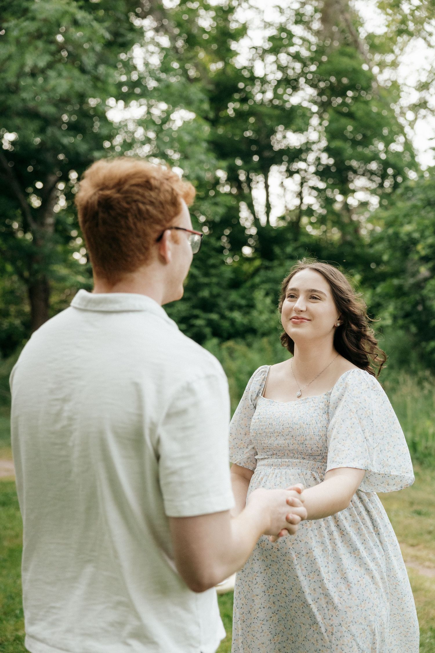 A couple shares joyful moments together in a sunlit outdoor setting wearing white and floral attire.