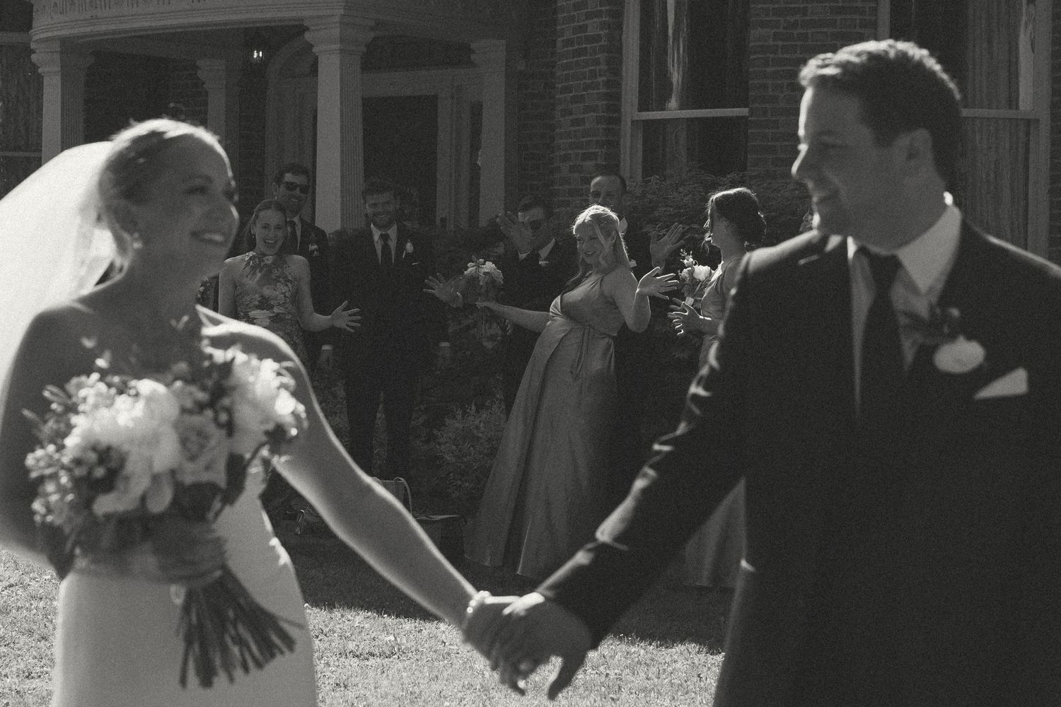 Black and white candid moment of newlyweds holding hands outdoors.