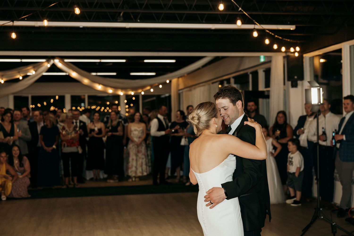 Couple shares their first dance under string lights at wedding reception.