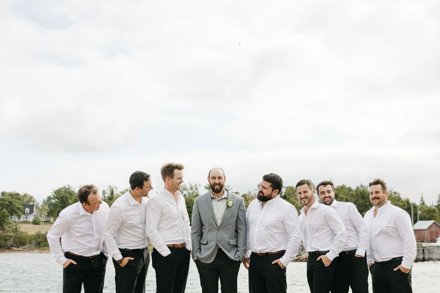 Groomsmen in white shirts and gray suits pose together outdoors.
