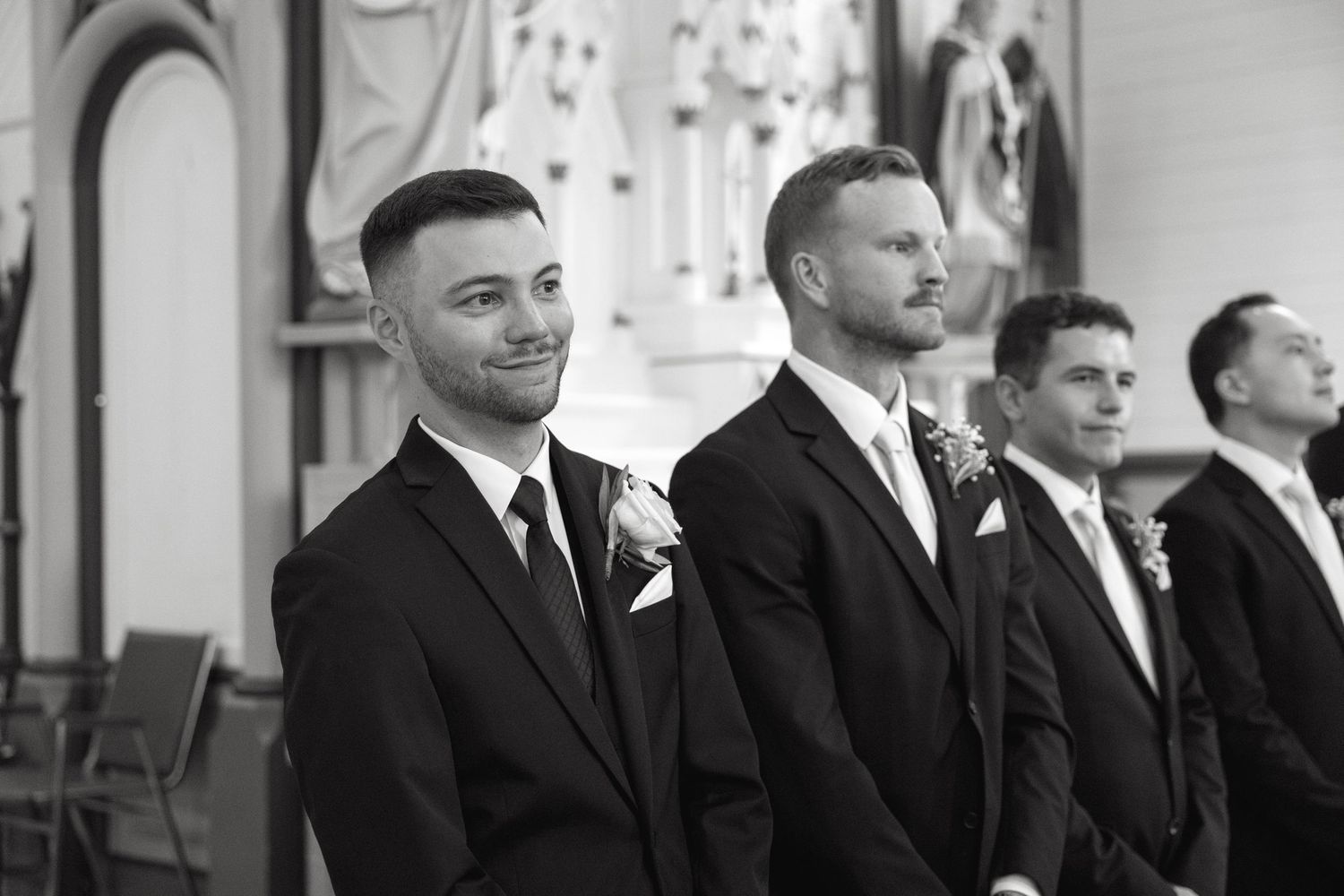 Groomsmen in black suits stand in a line during a formal ceremony.