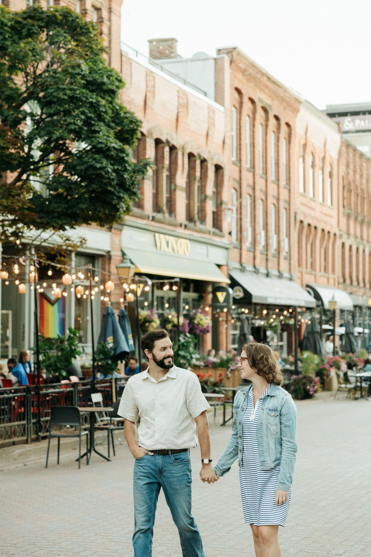Couple walking along historic brick storefront street with string lights overhead.