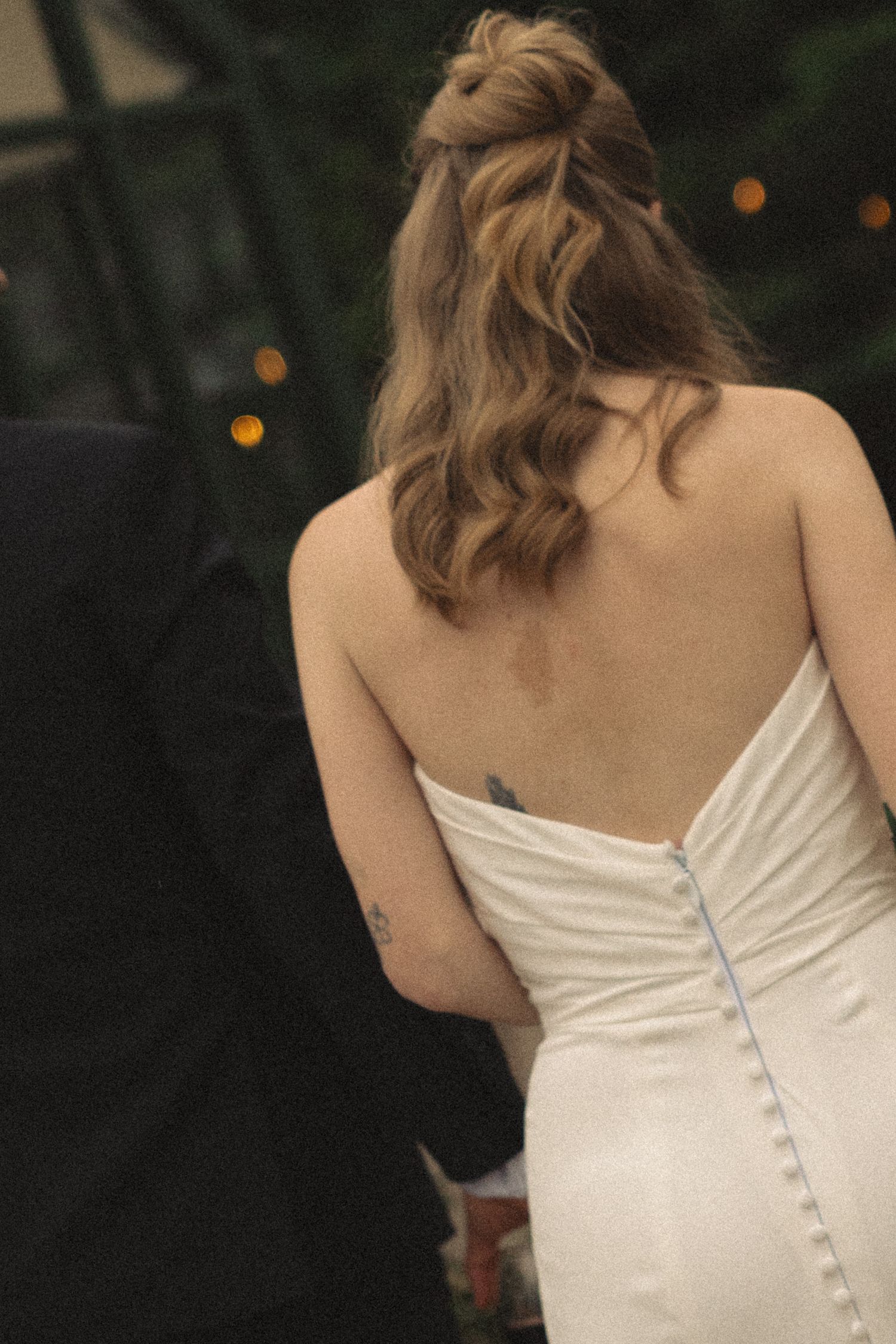 Close-up of bride's elegant strapless wedding gown with button back detail and soft wavy half-up hairstyle.