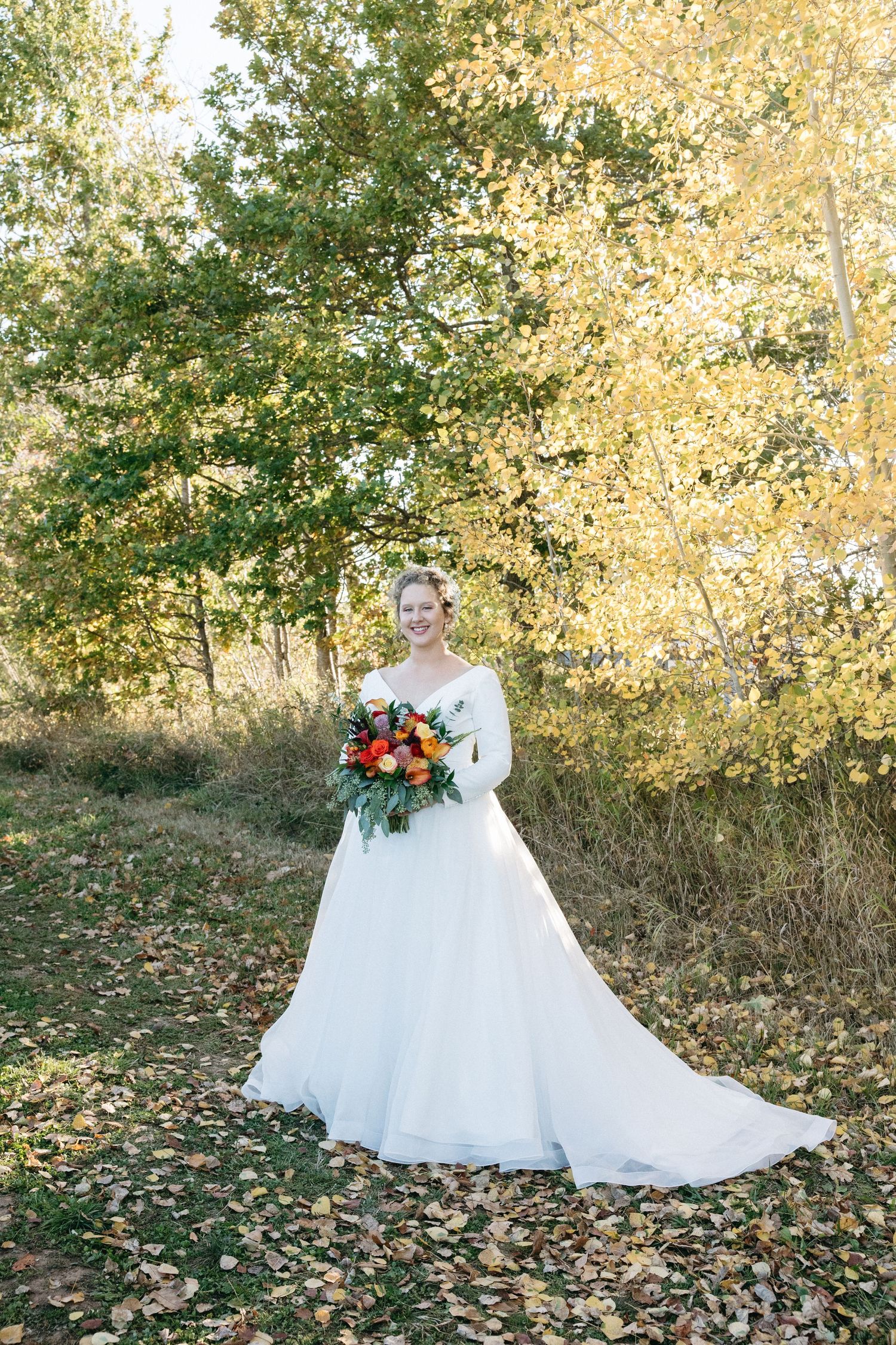 A flowing white wedding gown photographed in a scenic fall setting with golden leaves.
