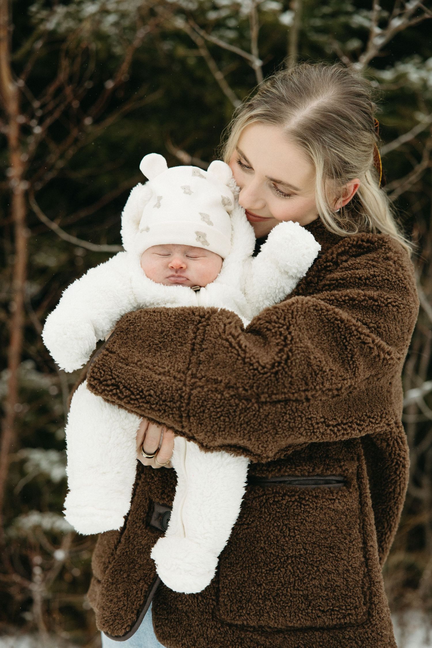 Tender winter moment with mother cradling baby in white snowsuit.