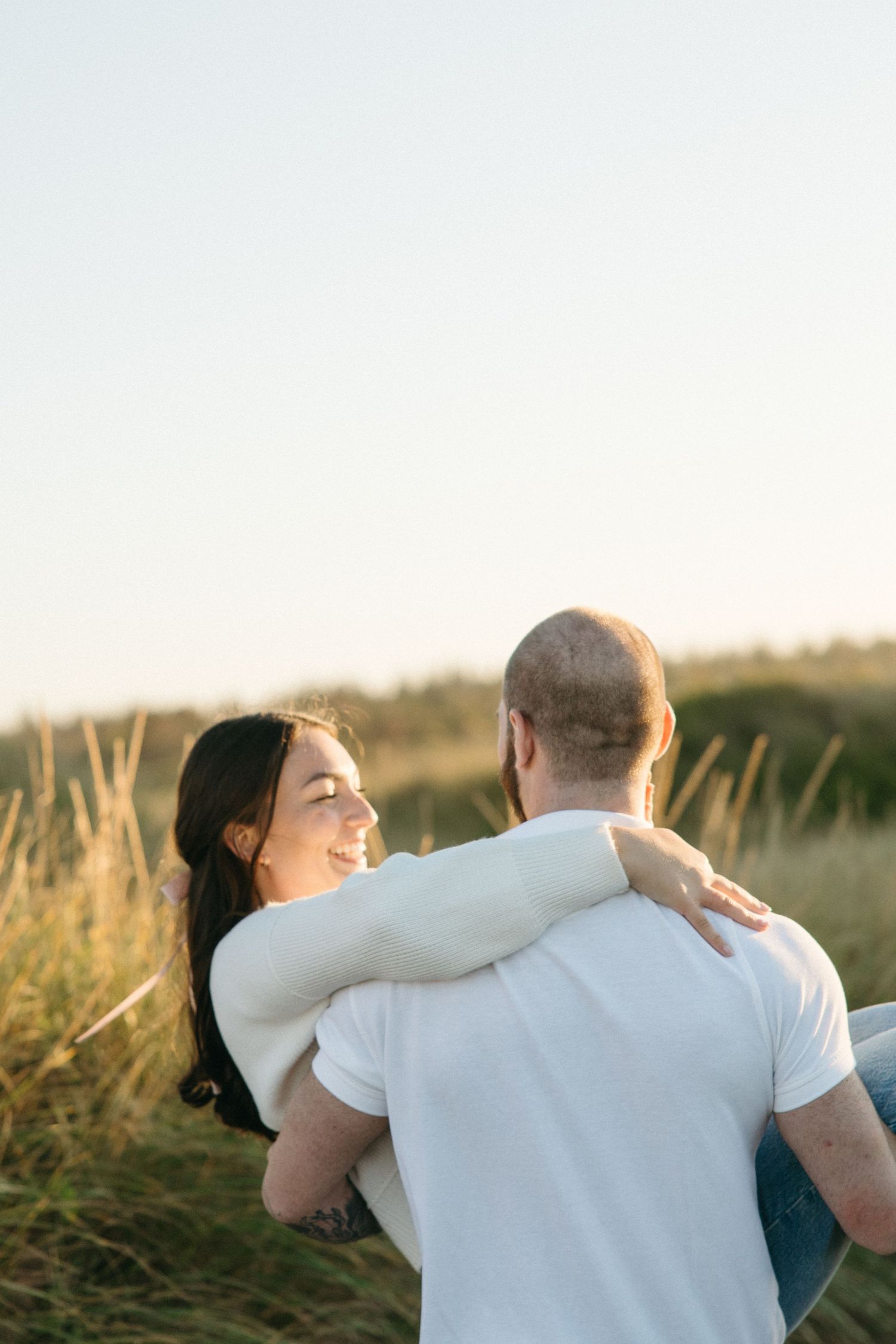 A couple shares a joyful moment while dancing in a grassy field at sunset.