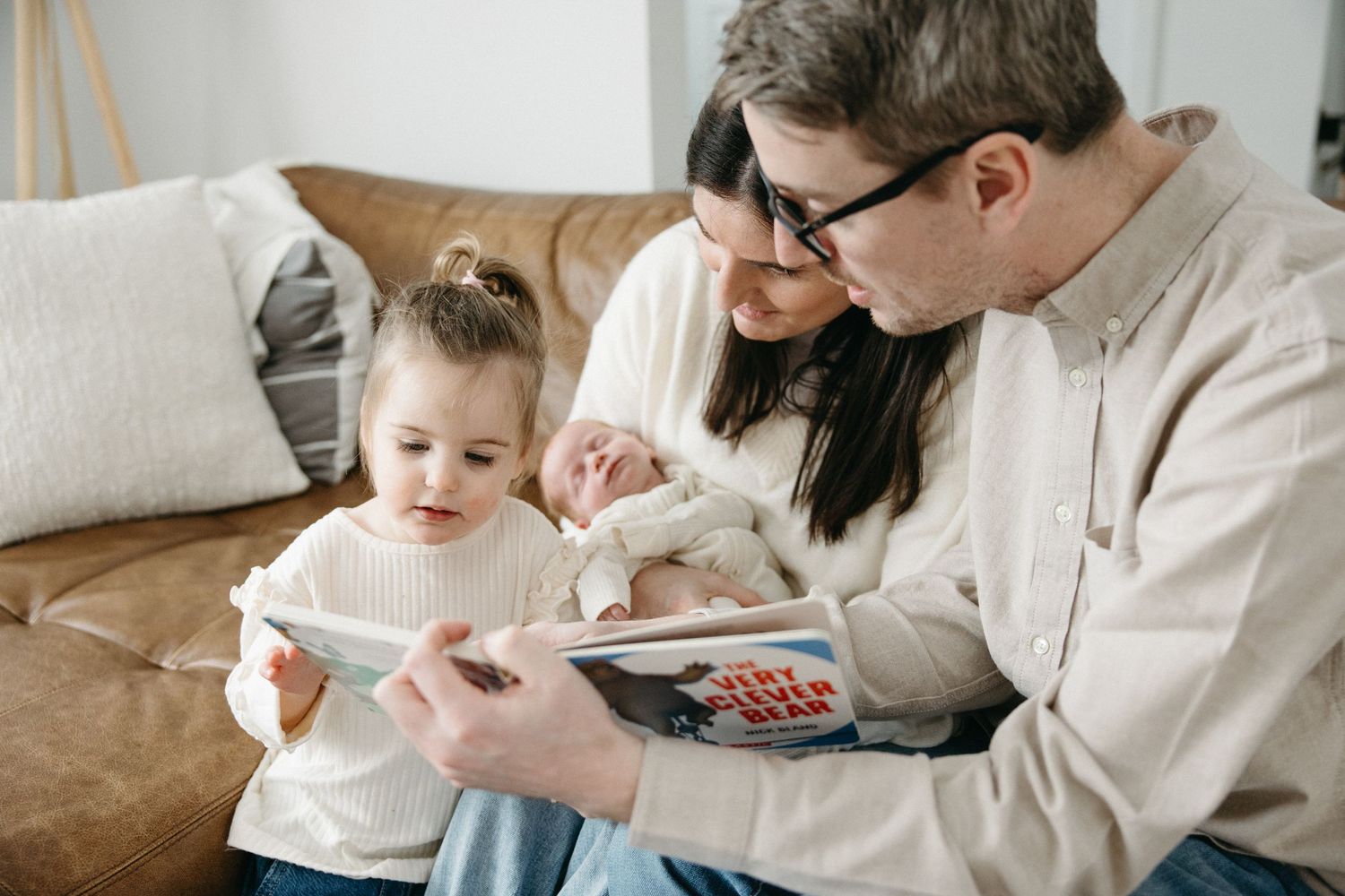 A family shares a tender moment together on a brown leather couch in a bright room.