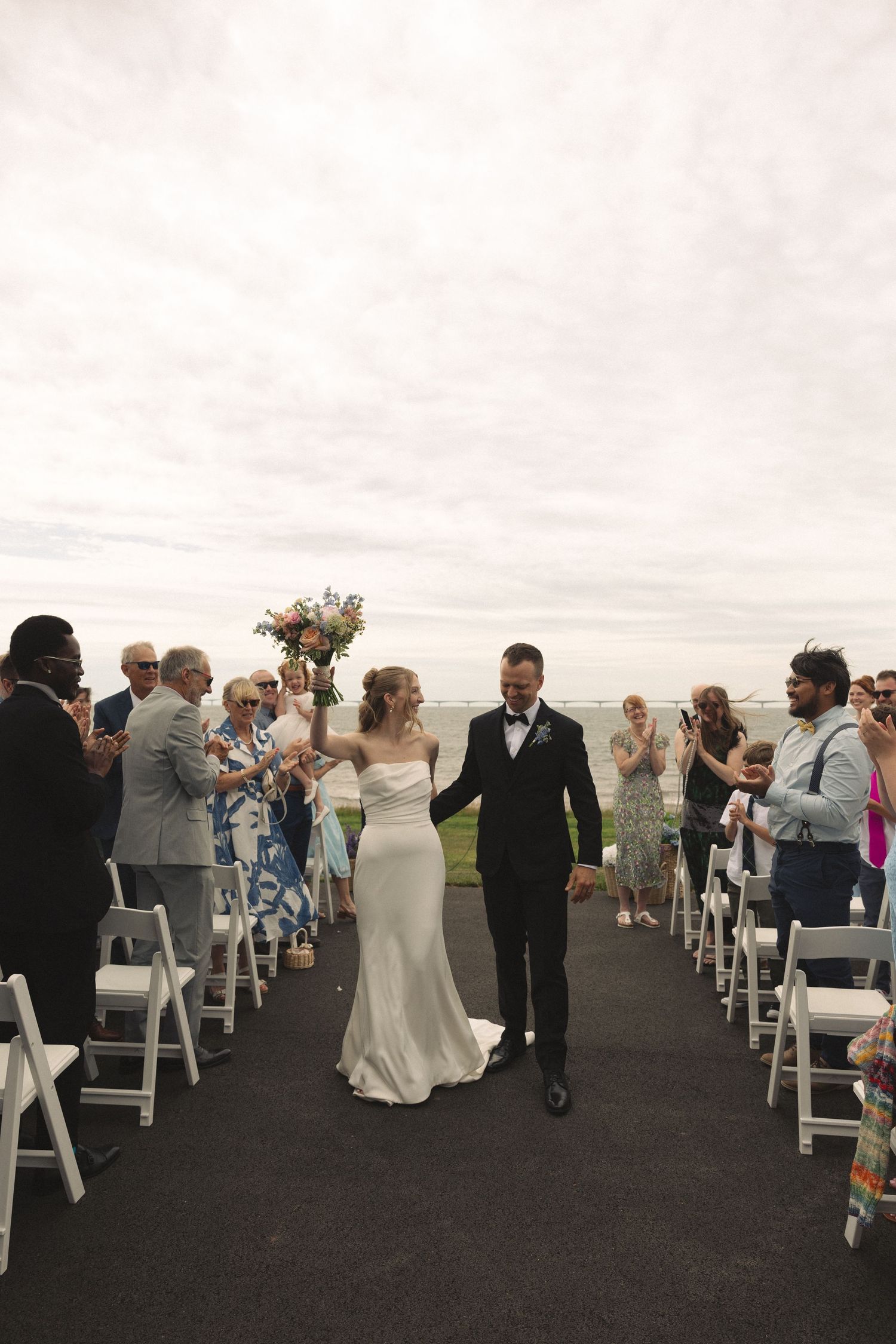Newlyweds walk back down the aisle after their outdoor wedding ceremony by the ocean.