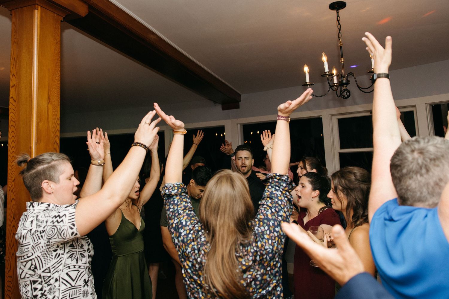 Wedding guests dancing with hands raised at lively indoor reception celebration.