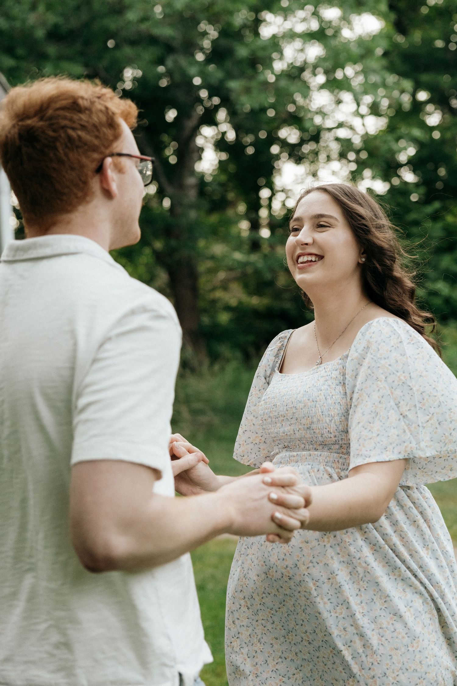 A couple dancing and laughing together in a sunlit garden wearing white and floral outfits.
