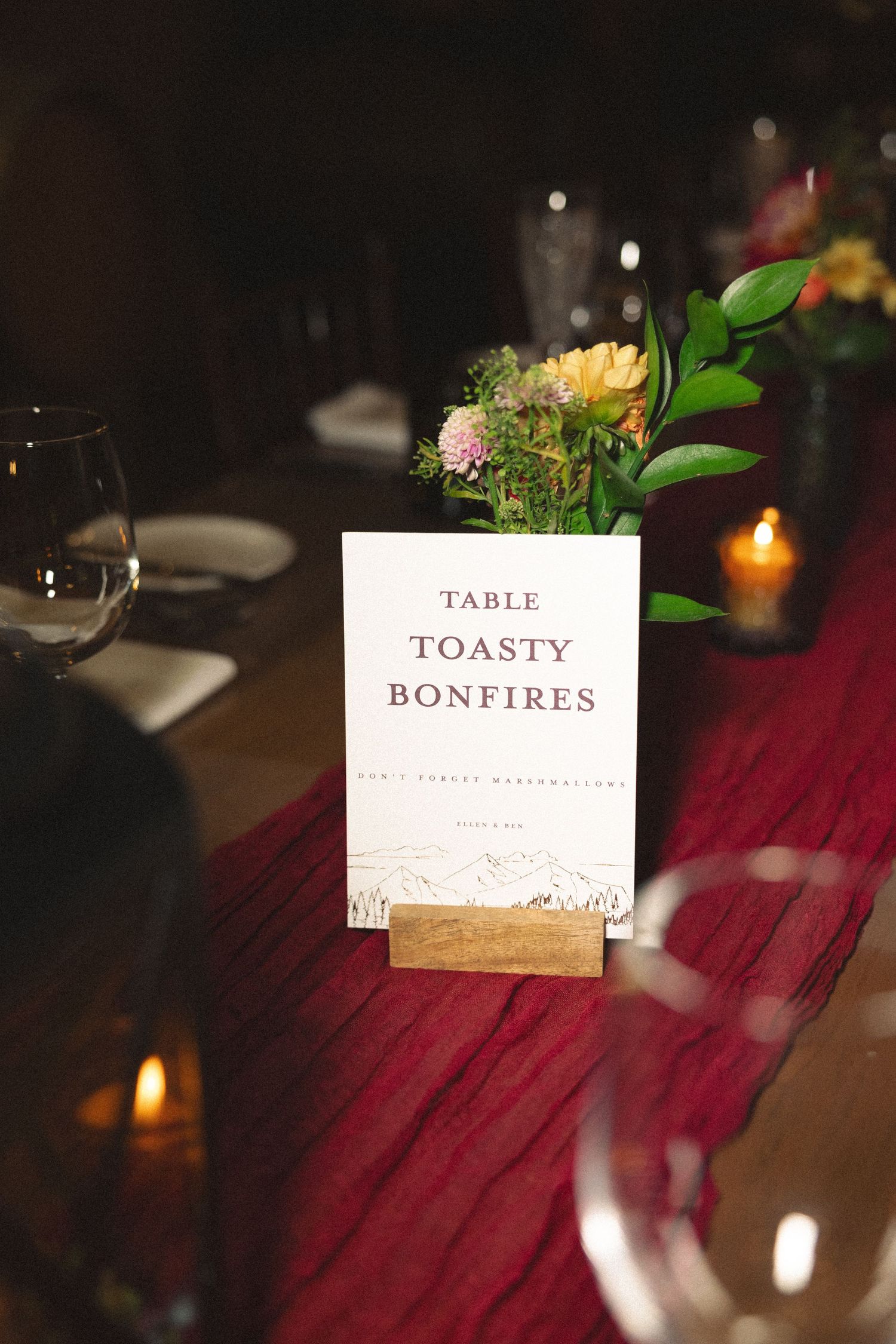 Wedding reception table cards reading 'Toasty' and 'Bonfires' with candlelight decor.