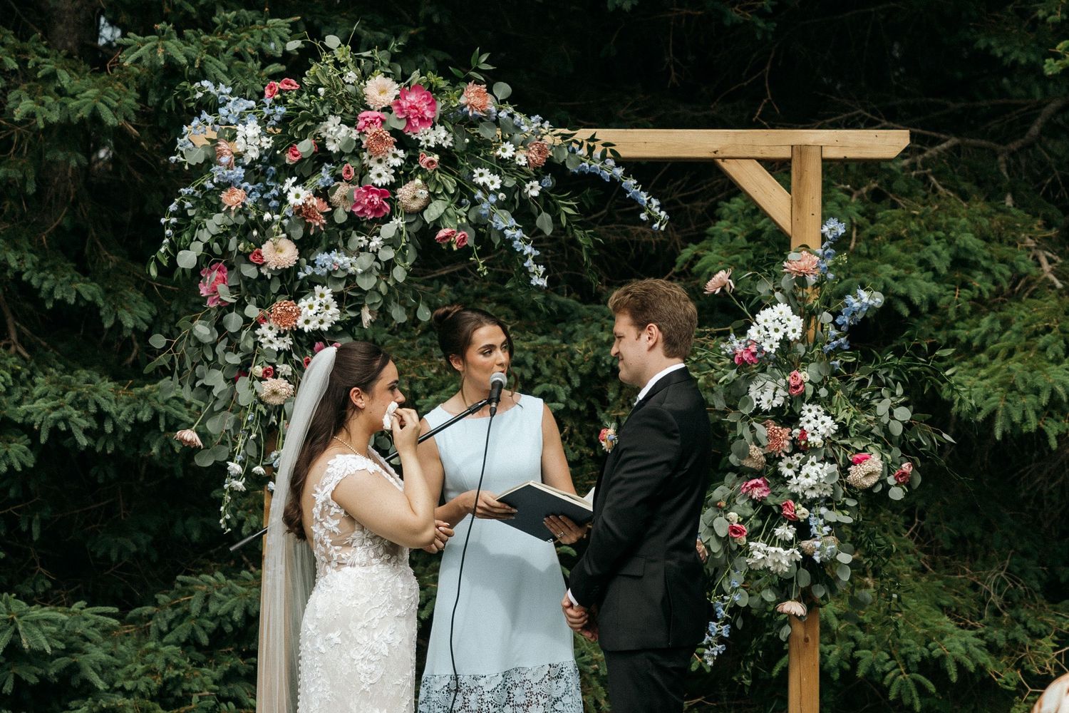 Wedding ceremony moments captured under wooden arch decorated with pink and white flowers.