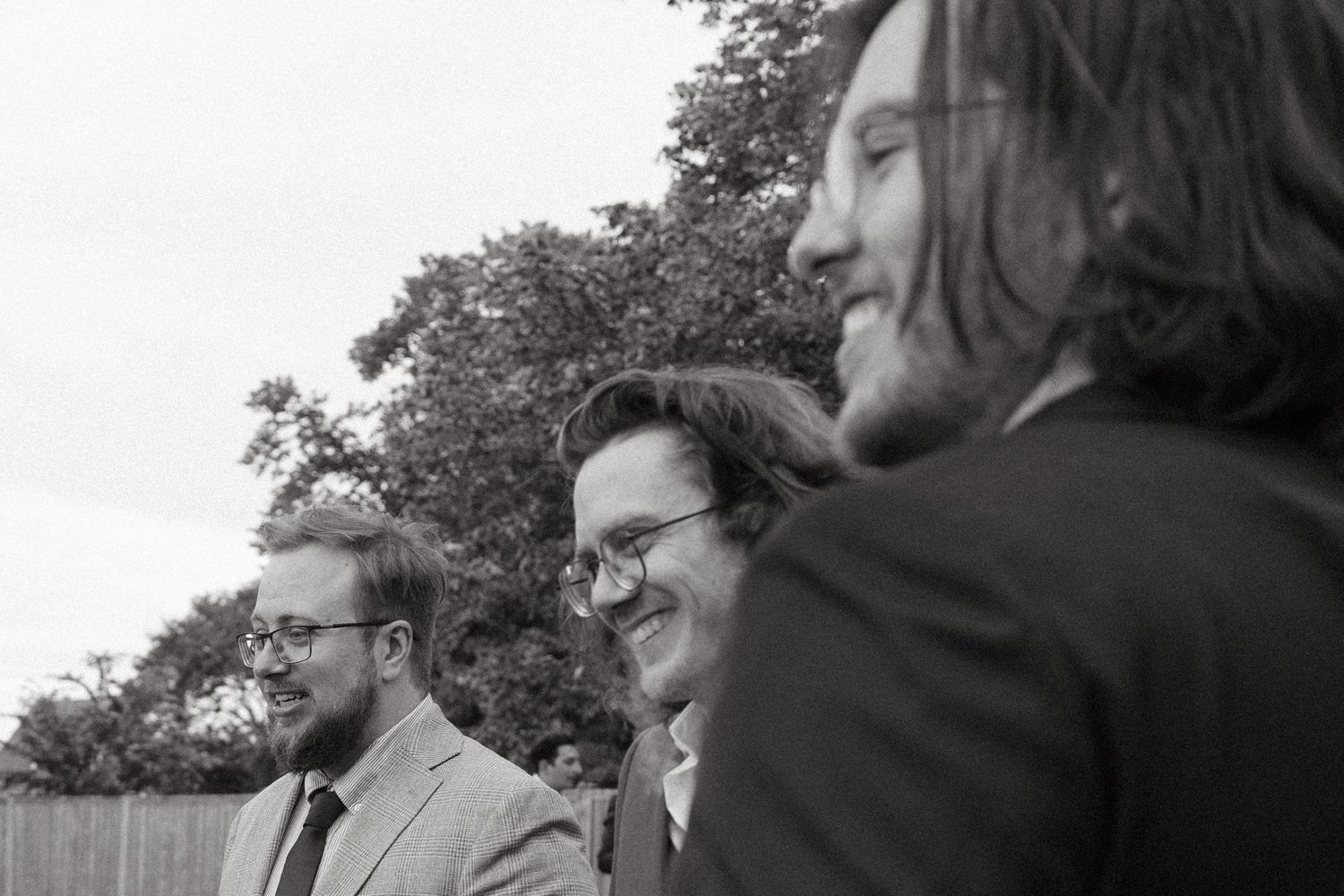A group of wedding guests gathered outdoors in formal attire.